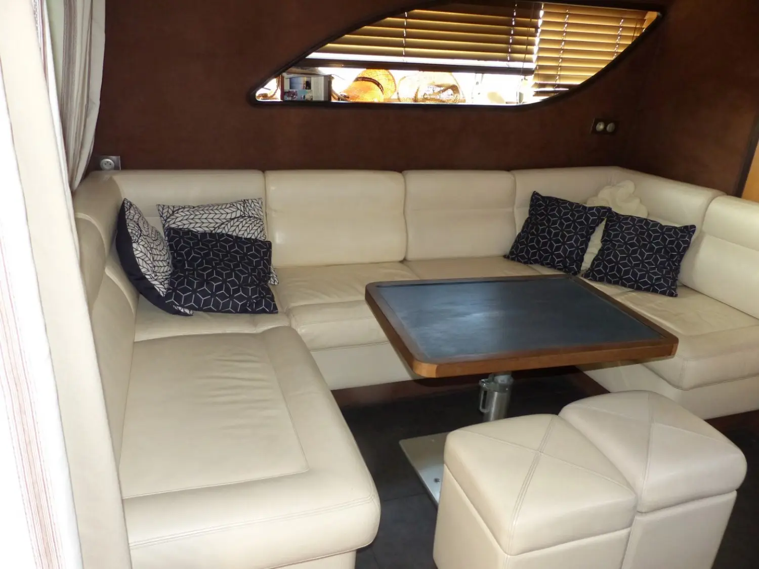 Mondomarine M 60 — Salon intérieur avec banquettes en cuir clair, coussins et table basse.