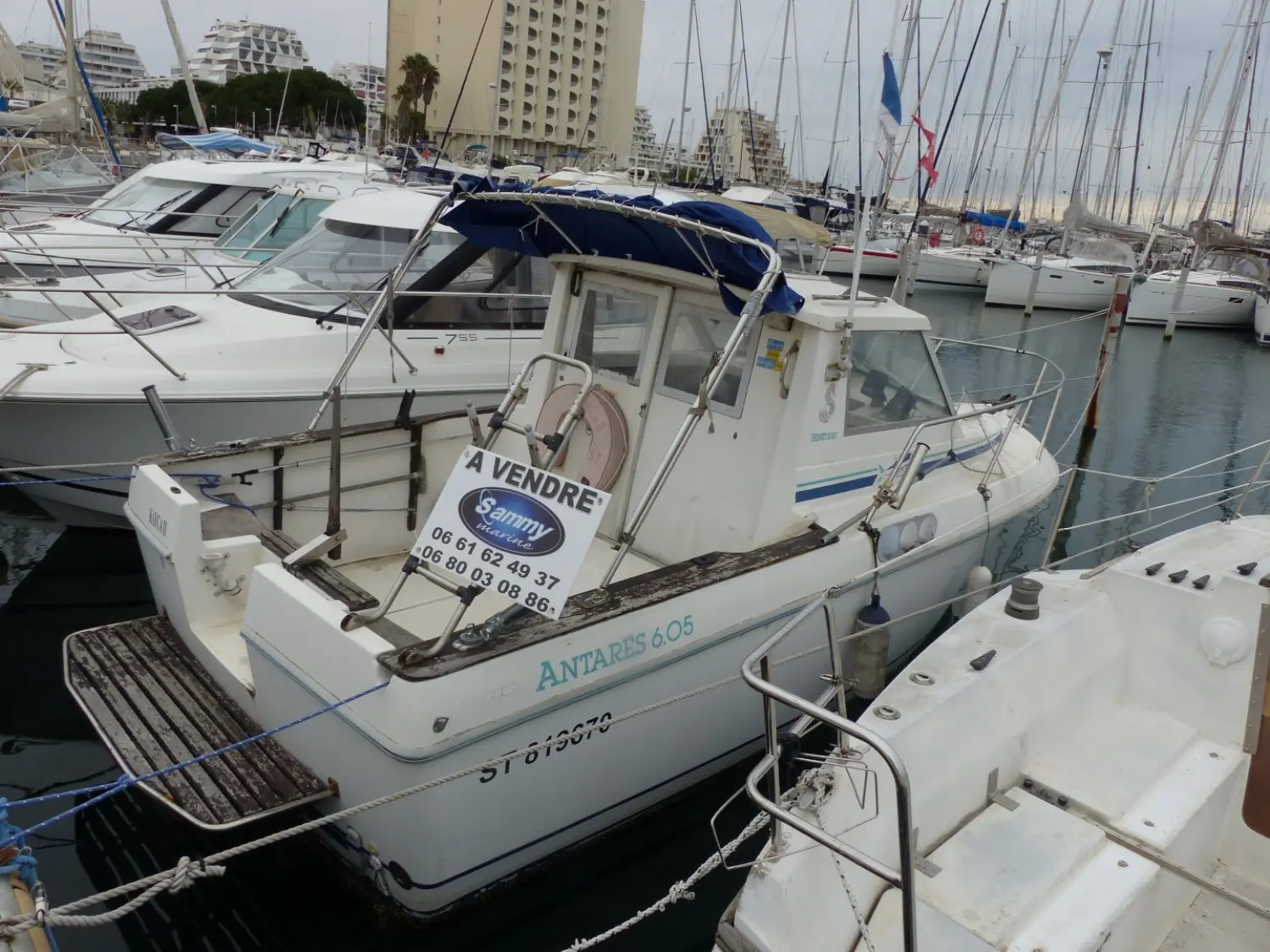 Beneteau Antares 605 — Vedette à moteur amarrée dans un port, avec un panneau « À VENDRE » visible.