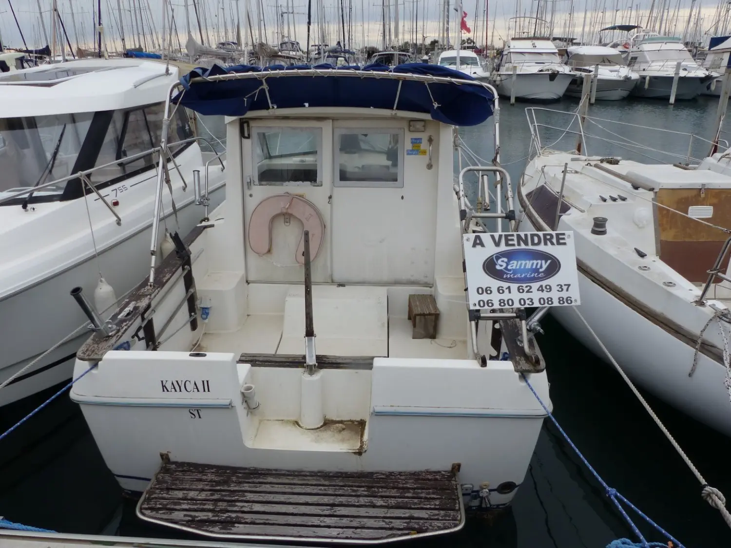 Beneteau Antares 605 — Vue arrière d’un bateau amarré dans un port, avec une affiche « À vendre ».
