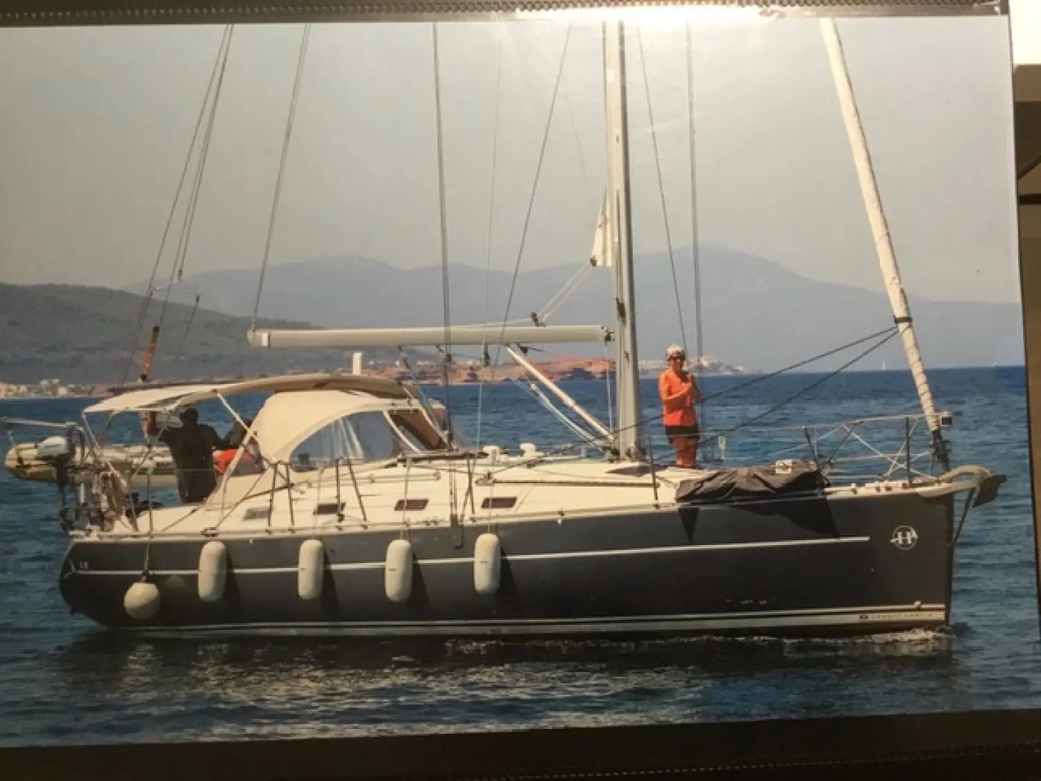 Harmony 38 — Voilier vu de profil sur l’eau, avec deux personnes à bord et des montagnes en arrière-plan.