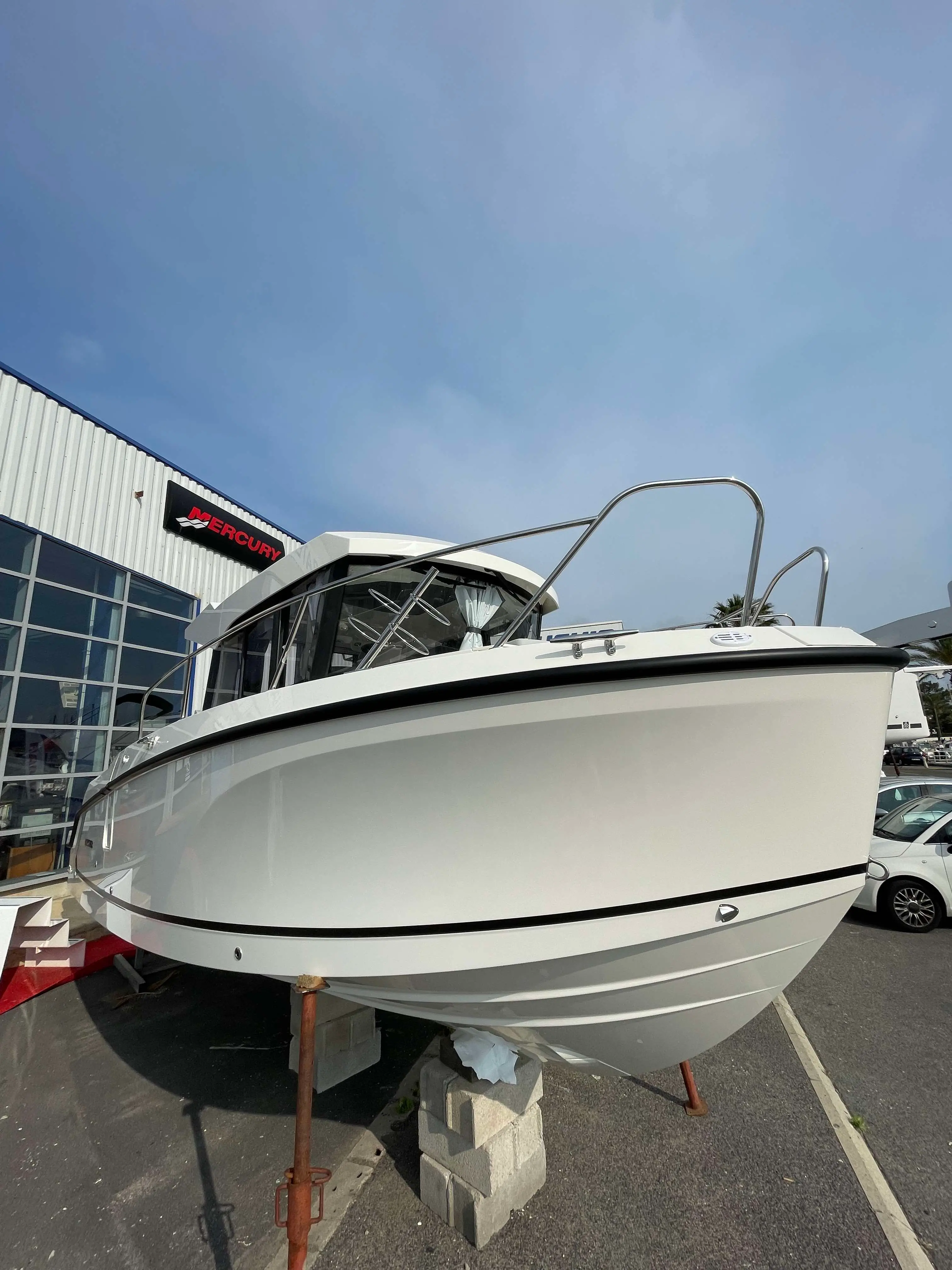 Quicksilver 805 Pilothouse — Vue avant trois quarts d’un bateau blanc exposé sur bers devant un bâtiment.