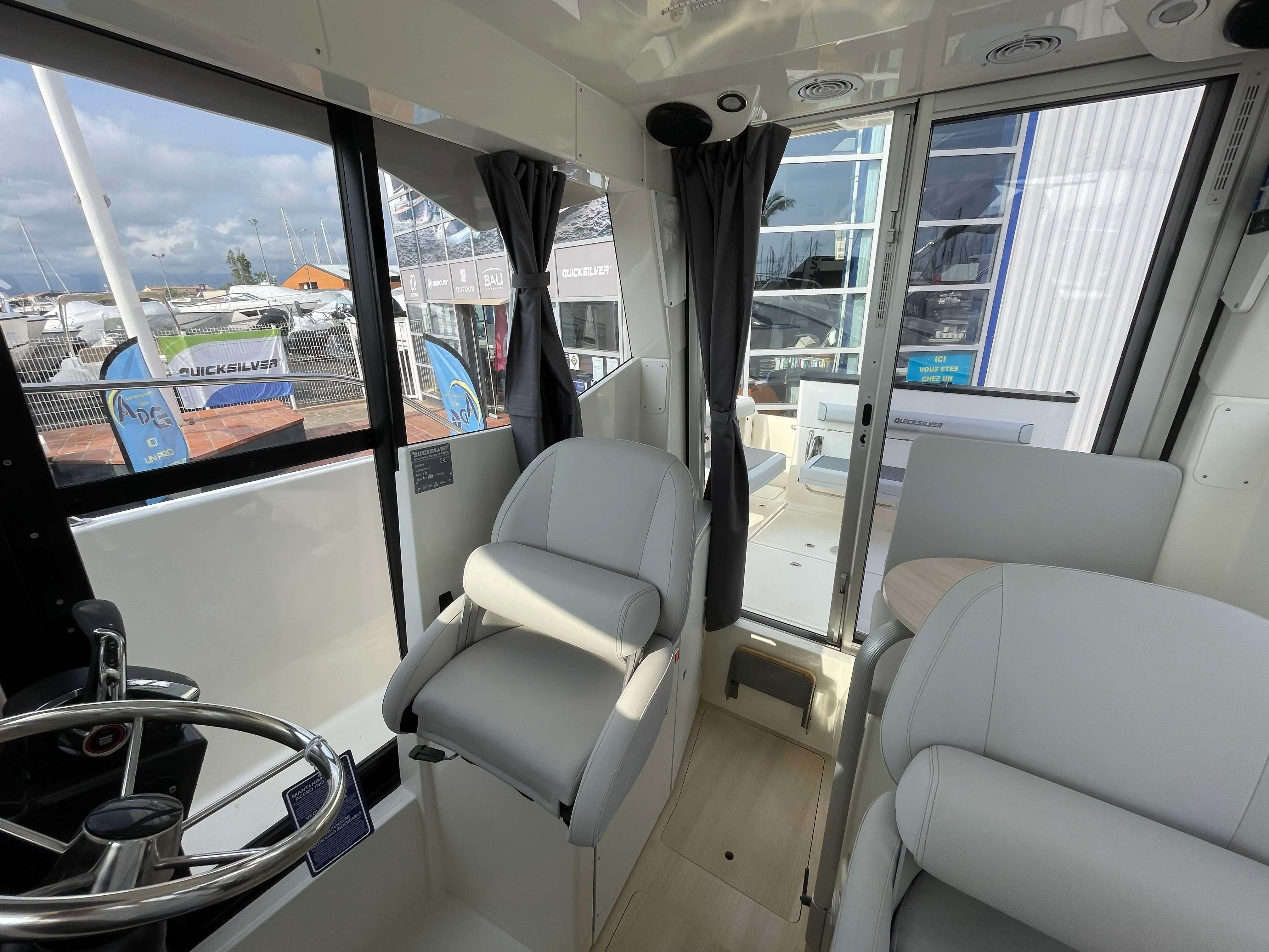 Quicksilver 805 Pilothouse — Vue intérieure du poste de pilotage, avec sièges, volant et accès au pont.