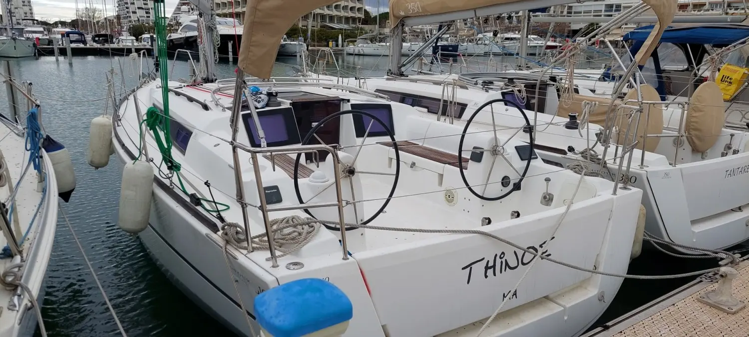 Dufour 310 — Voilier blanc amarré, vu de trois quarts arrière dans un port.