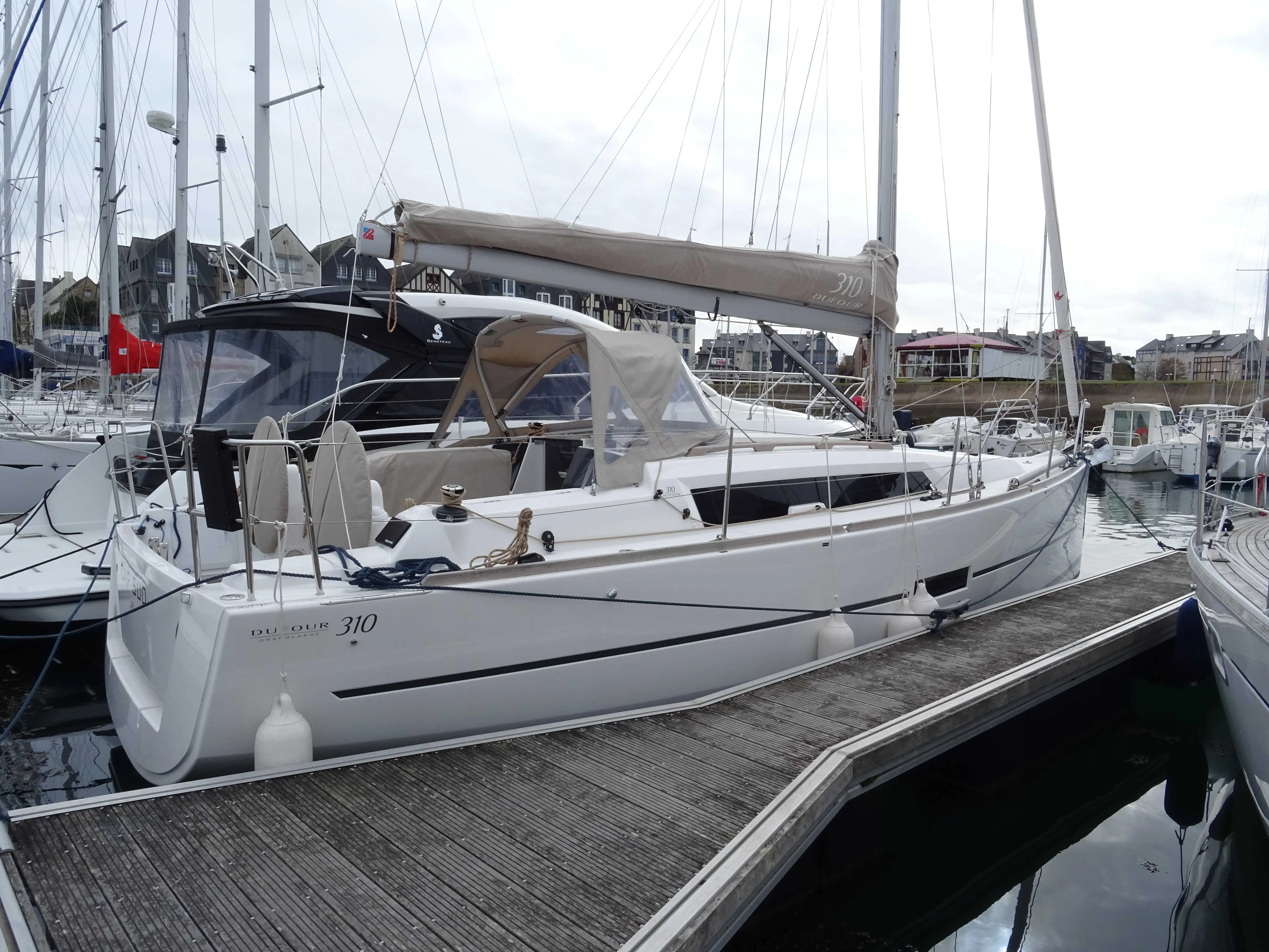 Dufour 310 — Voilier blanc amarré à un ponton, vu de trois quarts par temps couvert.