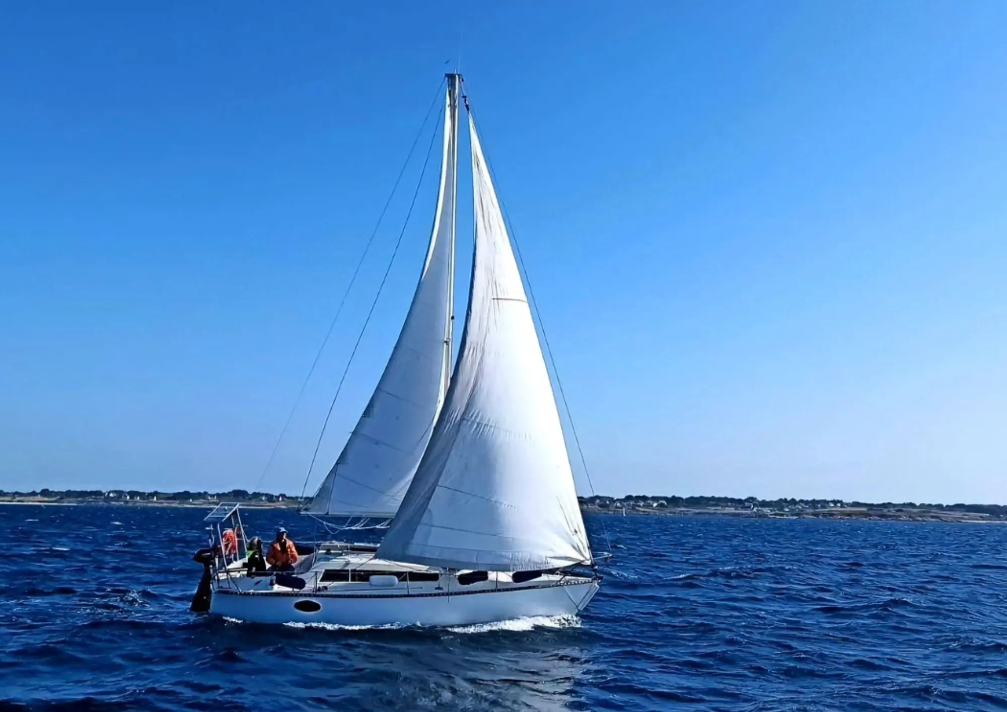 Yachting France Jouet 760 — Voilier blanc naviguant sous voiles au large, avec deux personnes à bord.