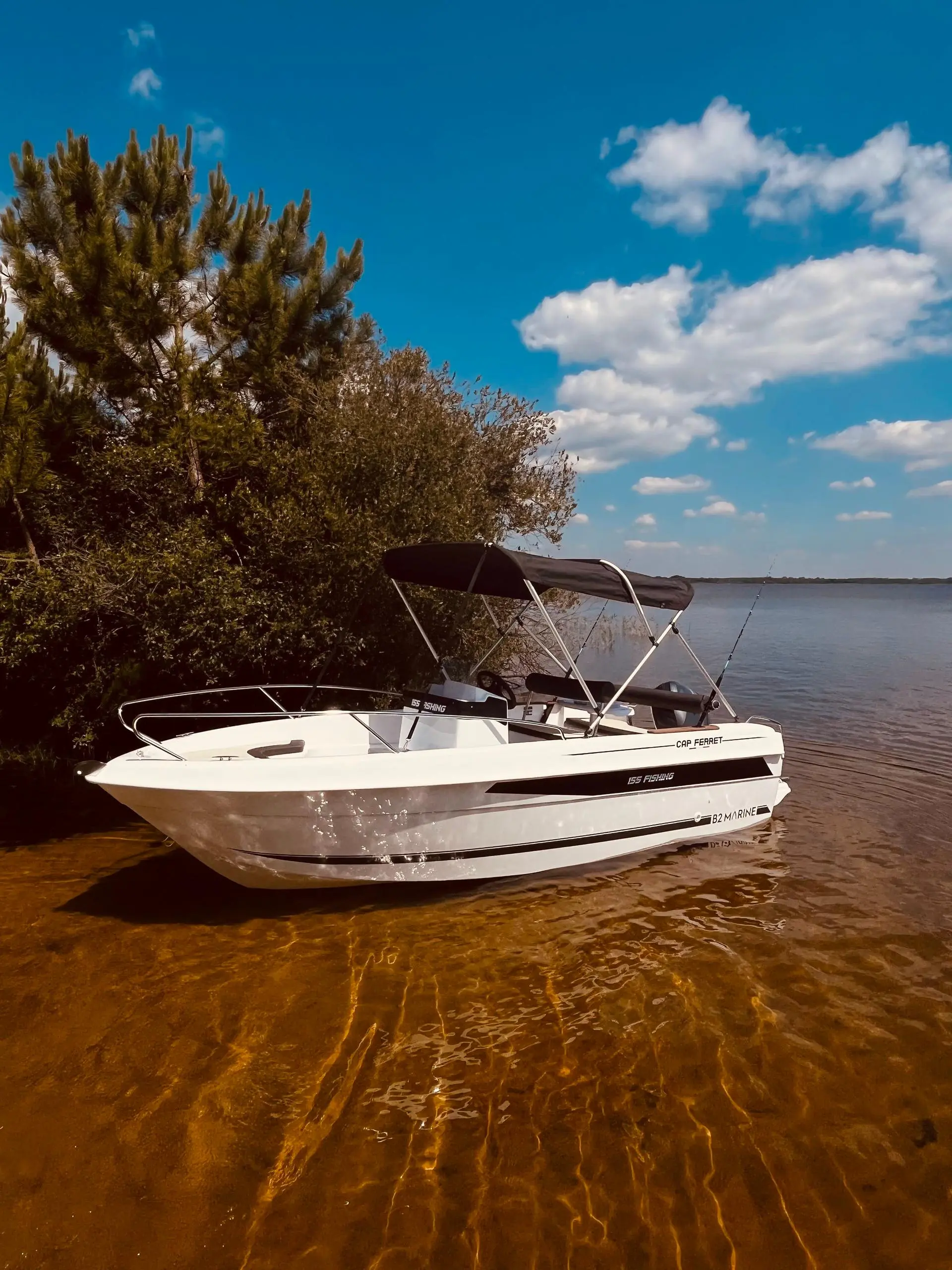 B2 Marine 155 — Bateau à moteur blanc amarré au bord d’un plan d’eau, sous un ciel nuageux.