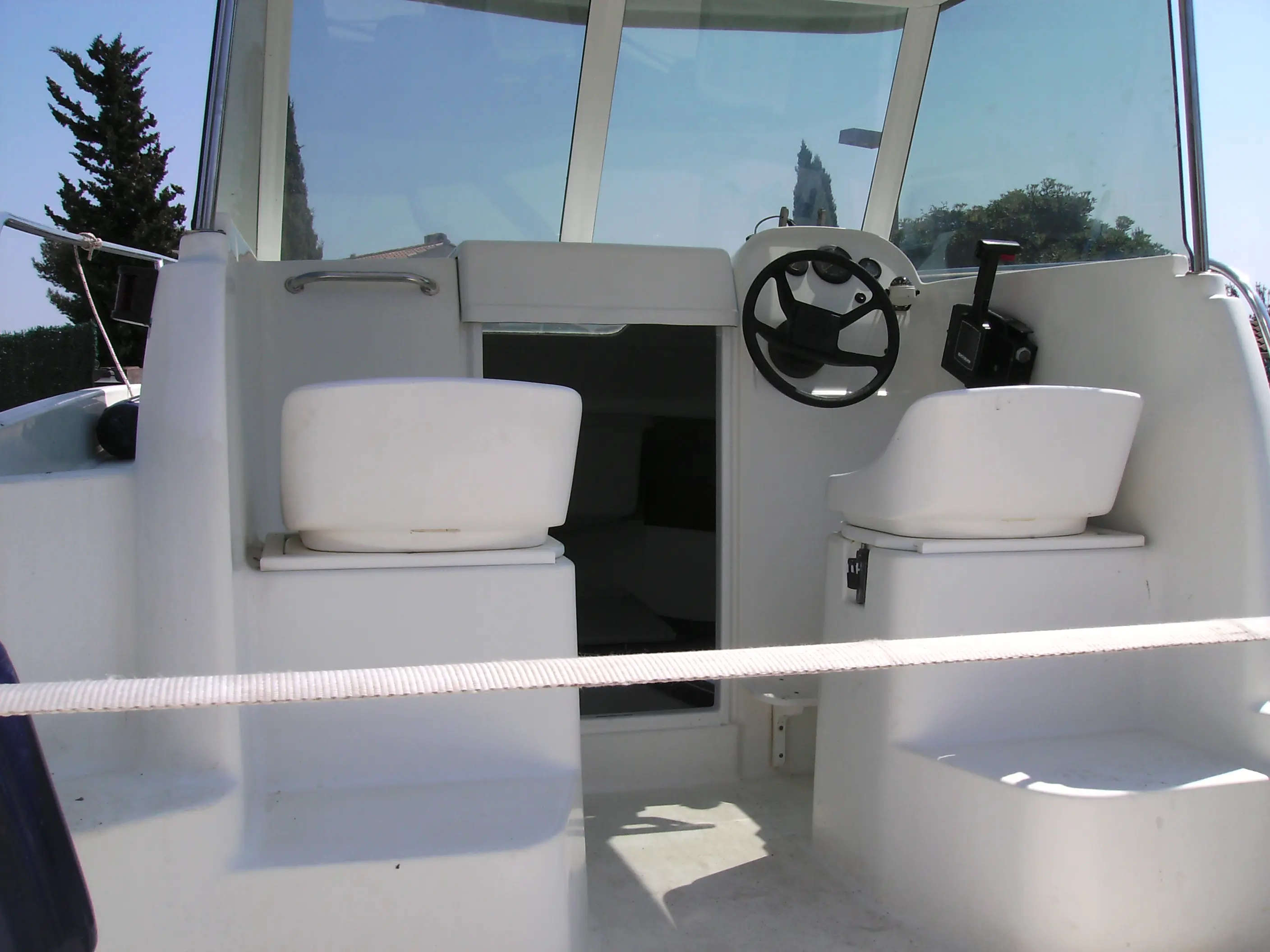 Jeanneau Merry Fisher 530 — Poste de pilotage avec volant, commandes et deux sièges protégés par une timonerie.