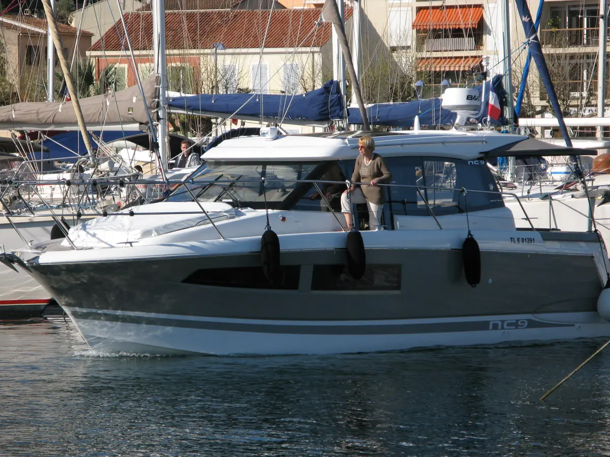Jeanneau NC 9 — Bateau à moteur blanc et gris amarré dans un port, vu de trois quarts.