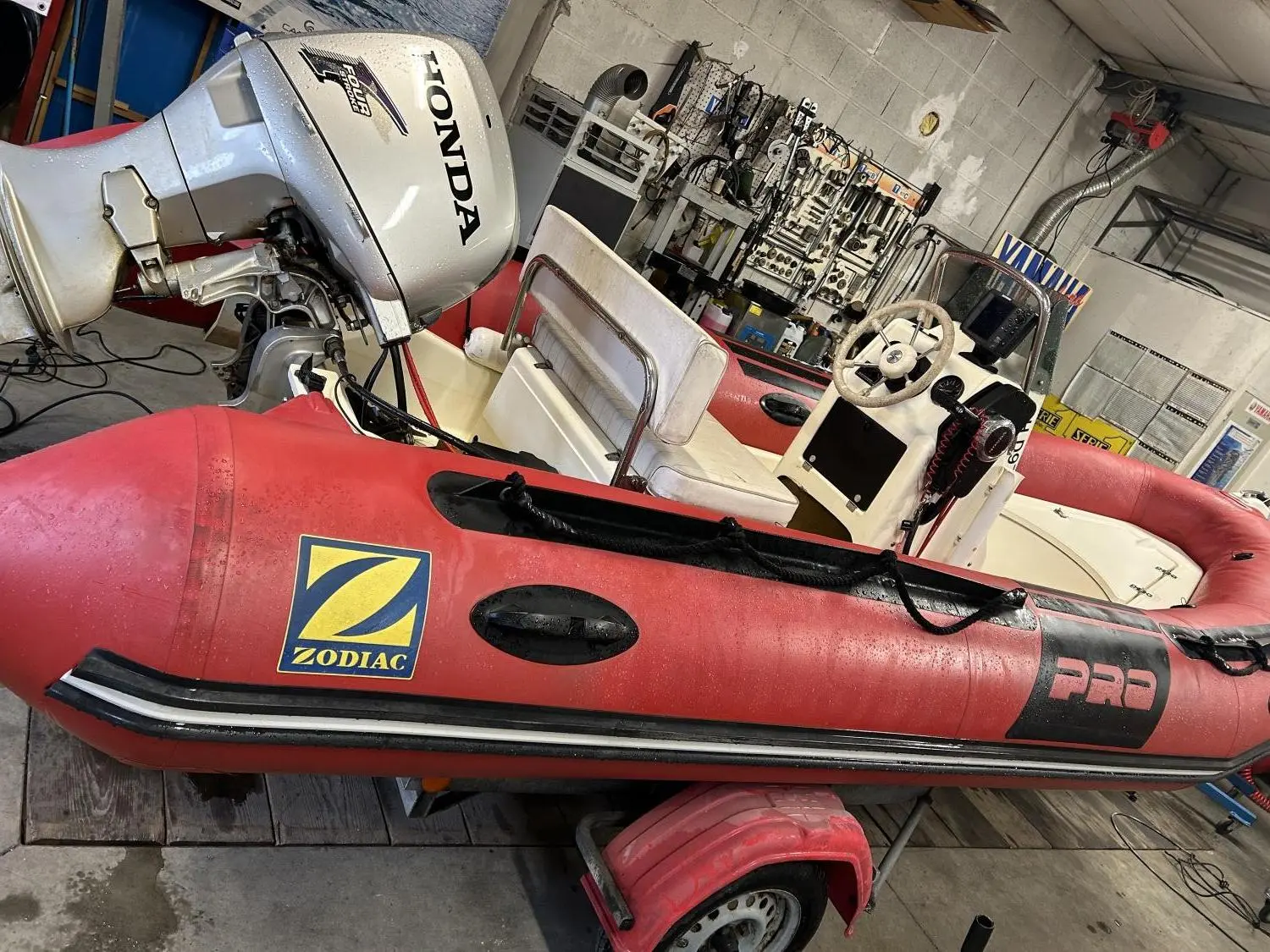 Zodiac Pro 9 Man — Semi-rigide rouge photographié dans un atelier, avec moteur hors-bord et console de pilotage.