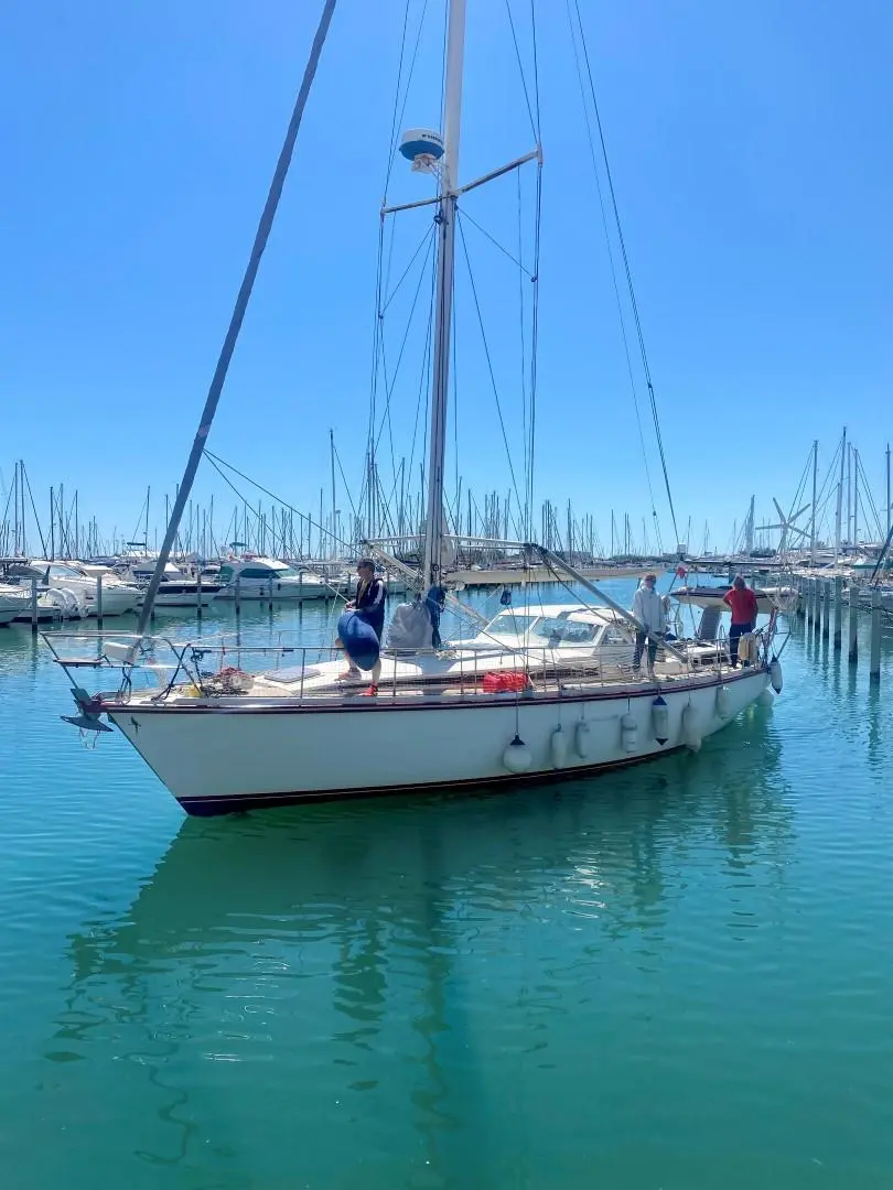Amel Santorin Sloop — Voilier blanc vu de trois-quarts dans un port de plaisance, avec plusieurs personnes à bord.