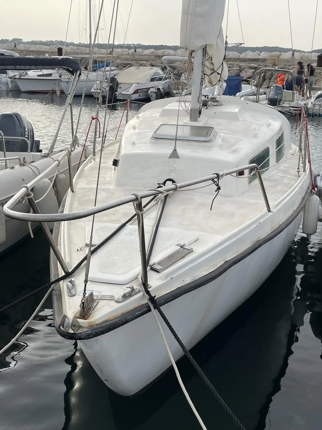 CNSO Daimio — Voilier blanc amarré, vu de l’avant dans un port, avec pont et cabine visibles.