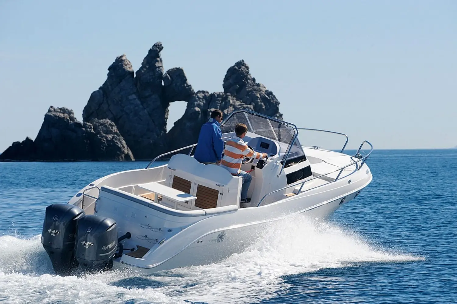 Pacific Craft 815 SC — Bateau à moteur blanc en navigation près d'un îlot rocheux, avec deux personnes à bord.