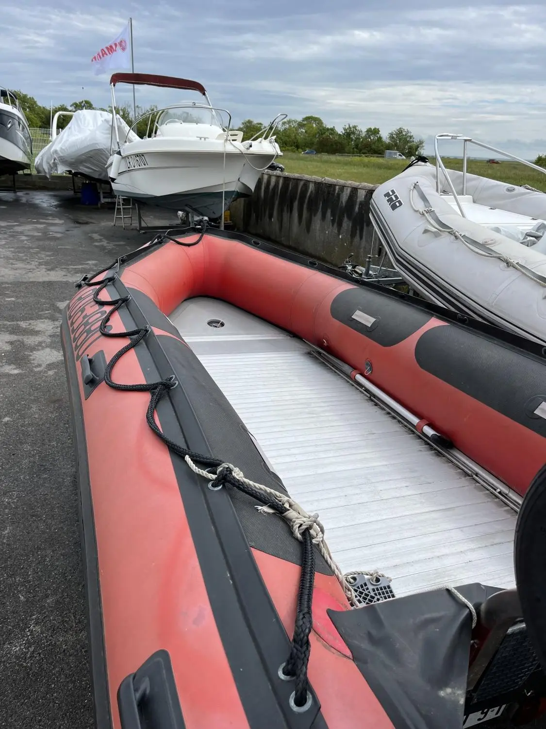 Quicksilver 420 Alu Rib — Un bateau pneumatique rouge au premier plan, devant plusieurs bateaux à terre.