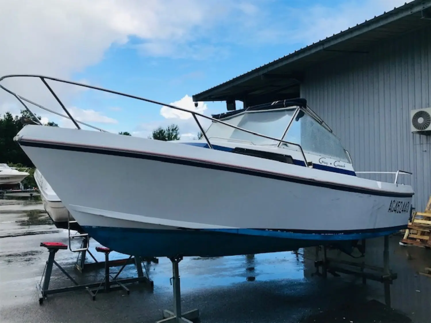 Guy Couach 580 — Bateau à moteur blanc et bleu photographié à terre devant un hangar.
