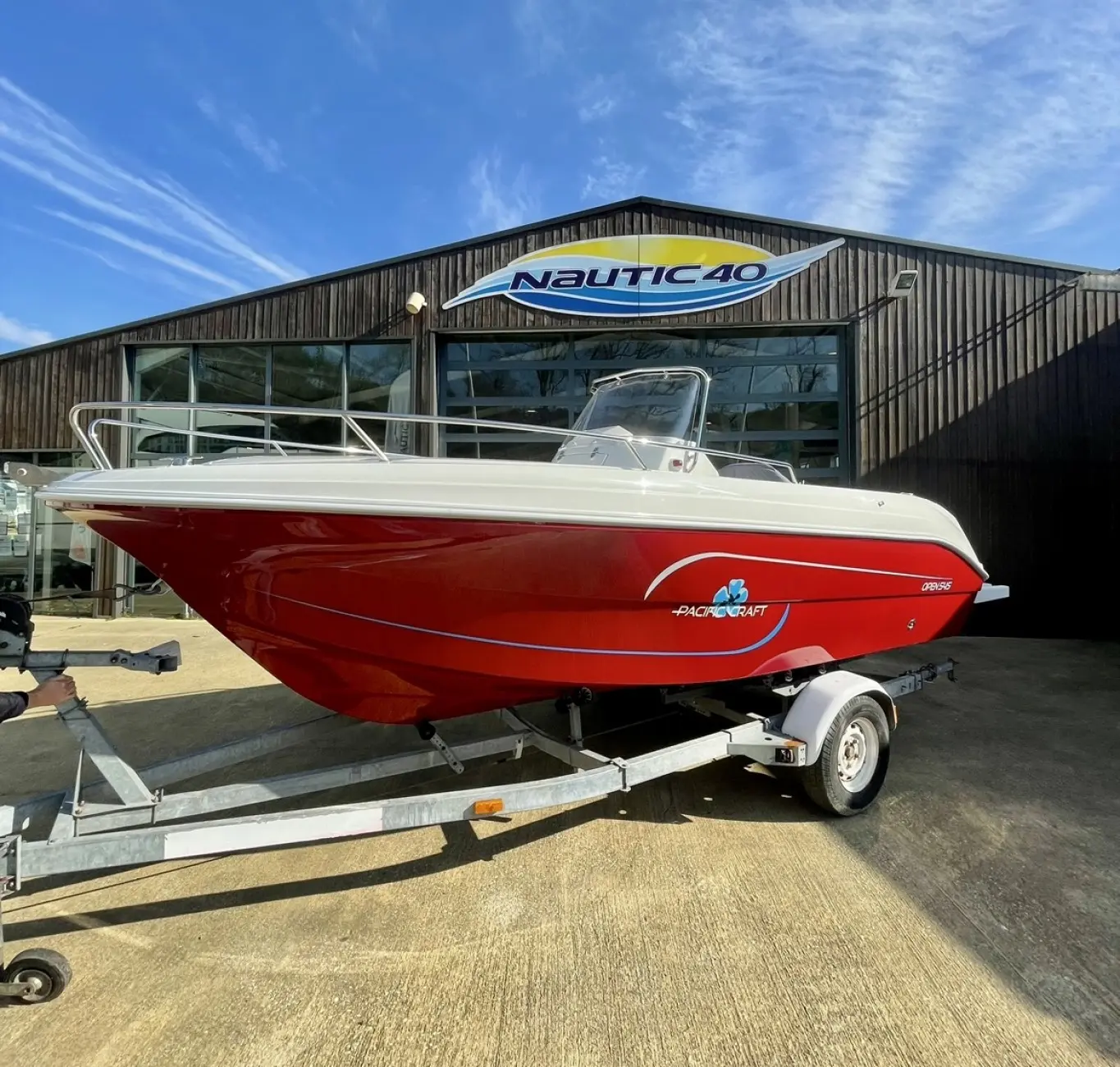 Pacific Craft 545 Trendy — Bateau à moteur rouge et blanc présenté sur remorque devant un concessionnaire.