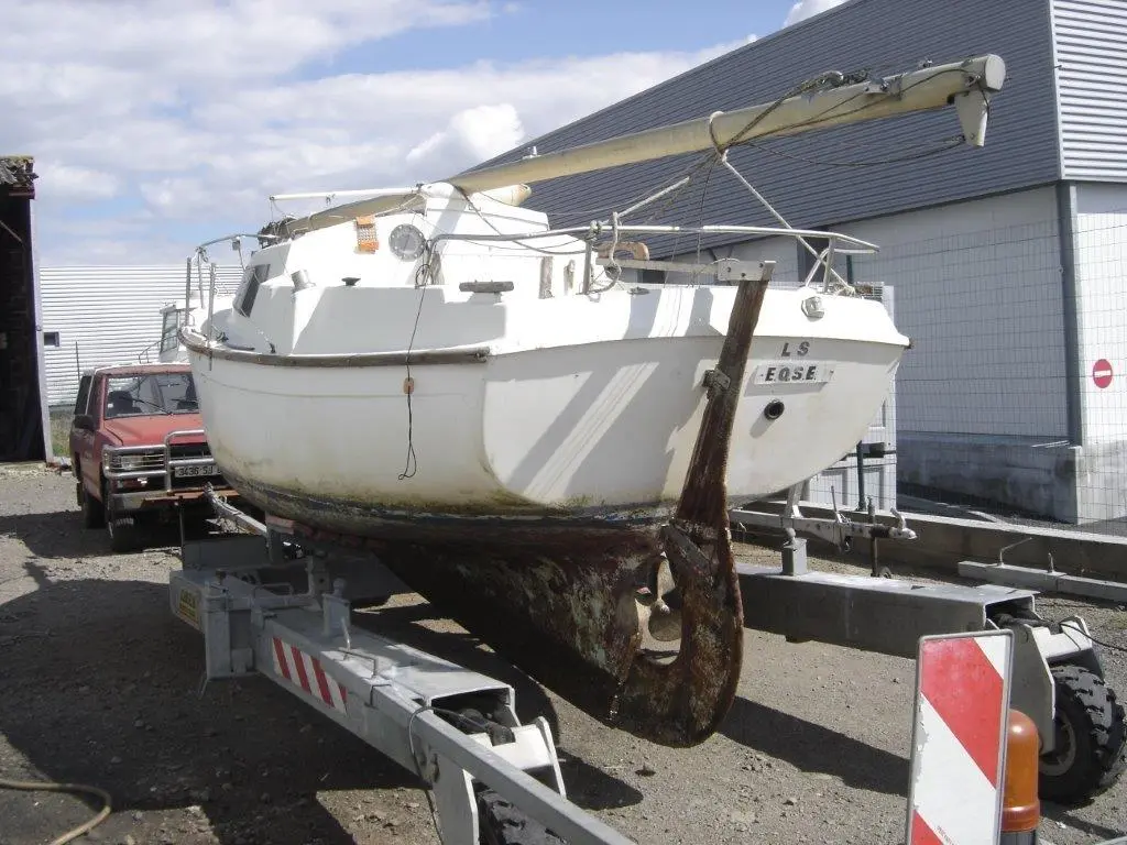 Beneteau Forban — Voilier blanc posé sur une remorque devant un bâtiment industriel.
