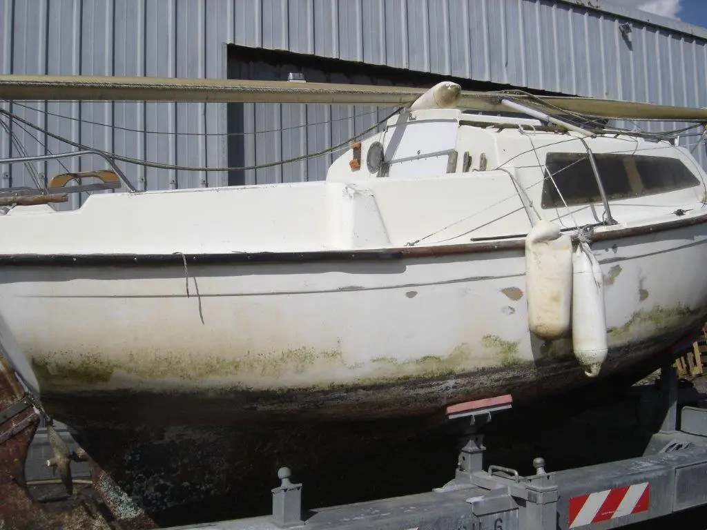 Beneteau Forban — Vue rapprochée d’un voilier blanc posé sur une remorque, devant un hangar.