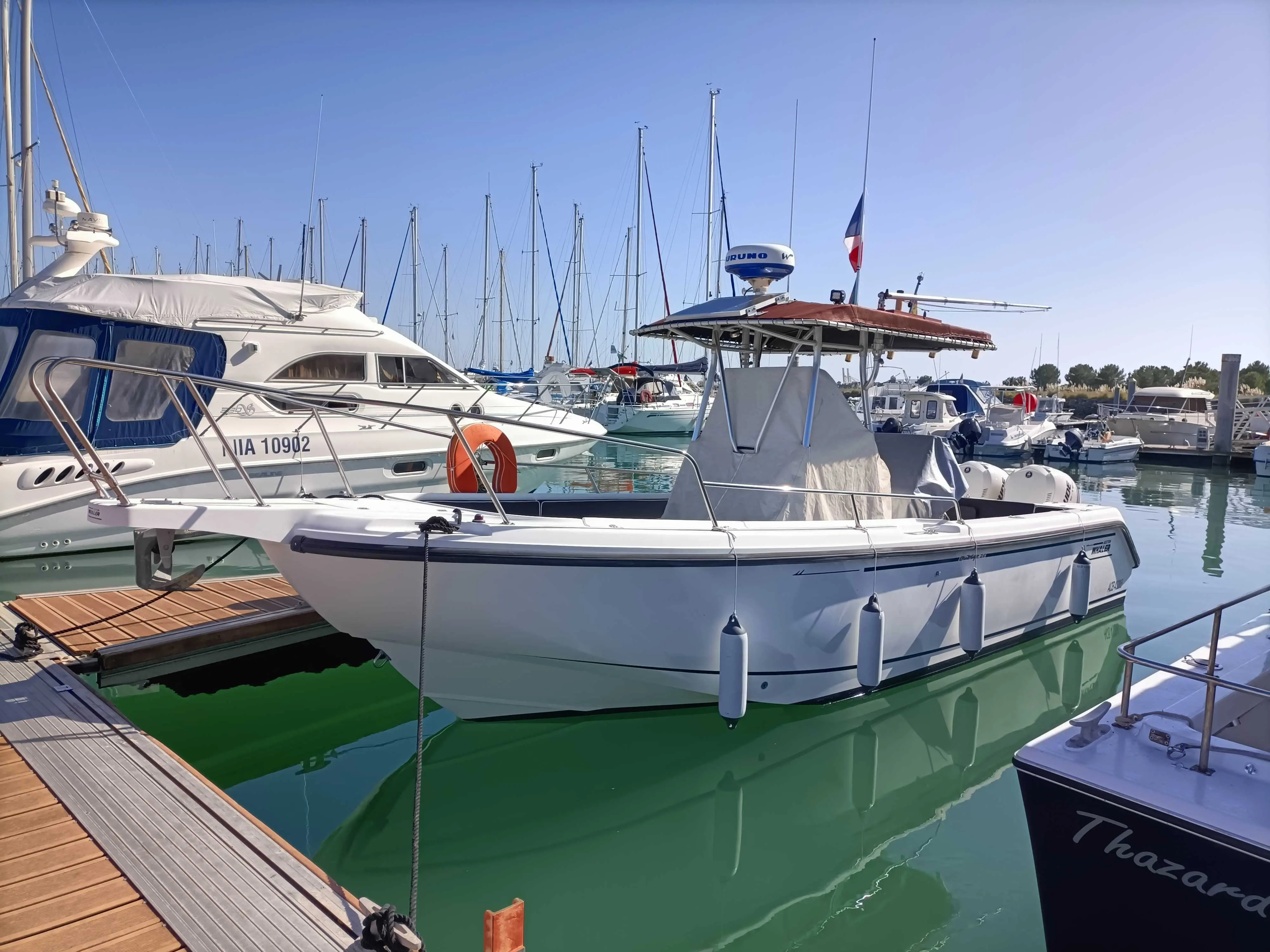 Boston Whaler 26 Outrage — Bateau à moteur blanc amarré dans une marina, avec taud et pare-battages.