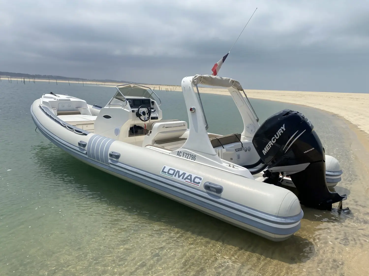 Lomac 790 IN — Bateau semi-rigide blanc amarré au bord d'une plage, vu de trois quarts arrière.