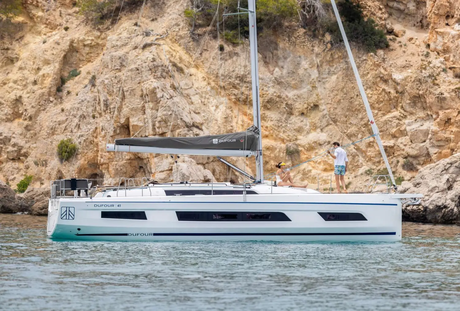 Dufour 41 — Voilier Dufour 41 vu de profil devant une côte rocheuse, avec deux personnes à bord.