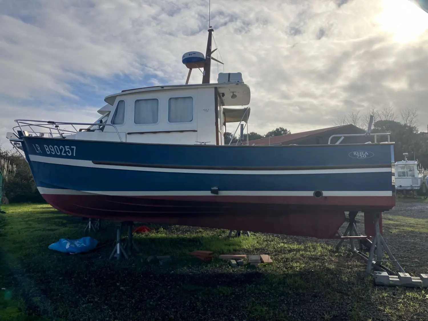 Rhea 750 — Bateau bleu et blanc vu de profil, à terre sur des bers, sous un ciel nuageux.