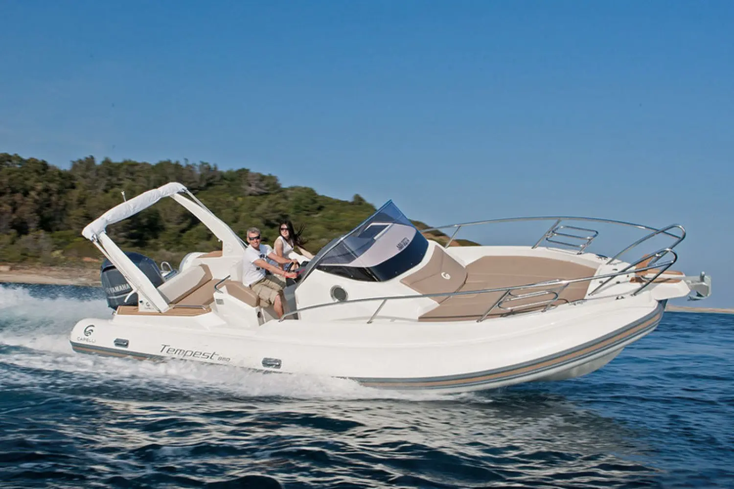 Capelli Tempest 850 — Bateau à moteur blanc naviguant près d’une côte boisée, avec deux personnes à bord.