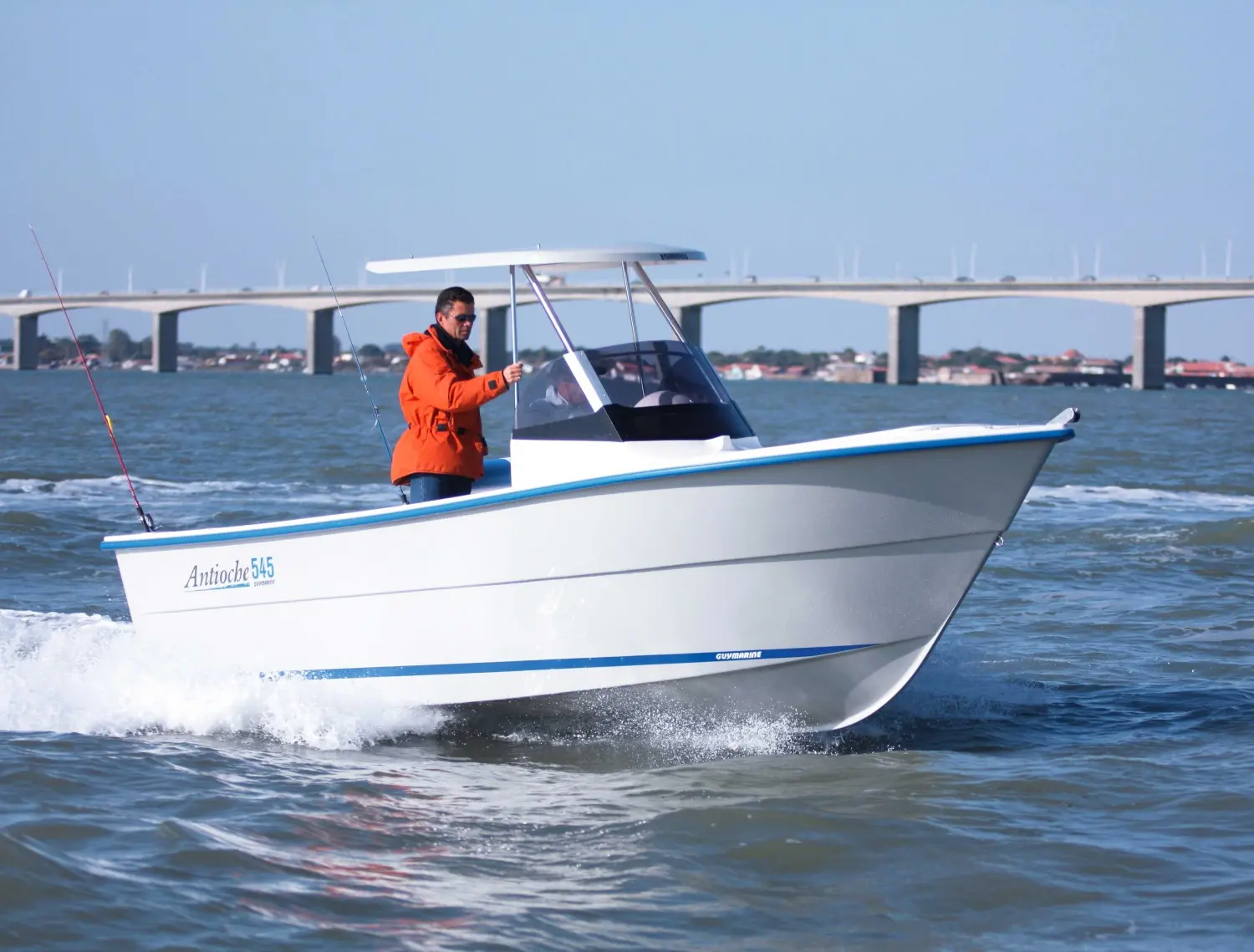 Guymarine Antioche 545 Cabine — Bateau à moteur blanc et bleu naviguant devant un long pont.