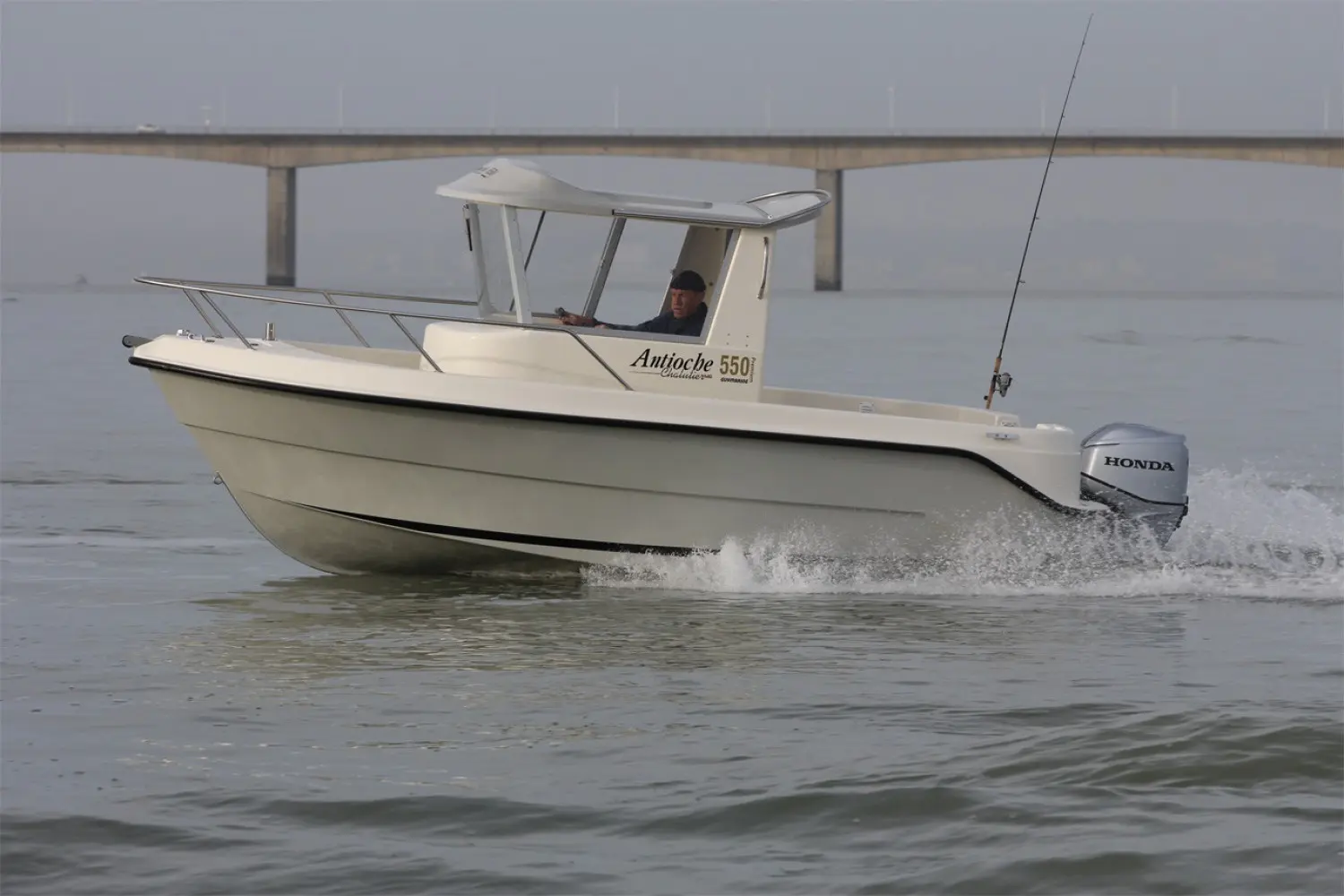 Guymarine Antioche 550 Chalutier — Bateau à moteur blanc naviguant devant un pont, vu de trois quarts.