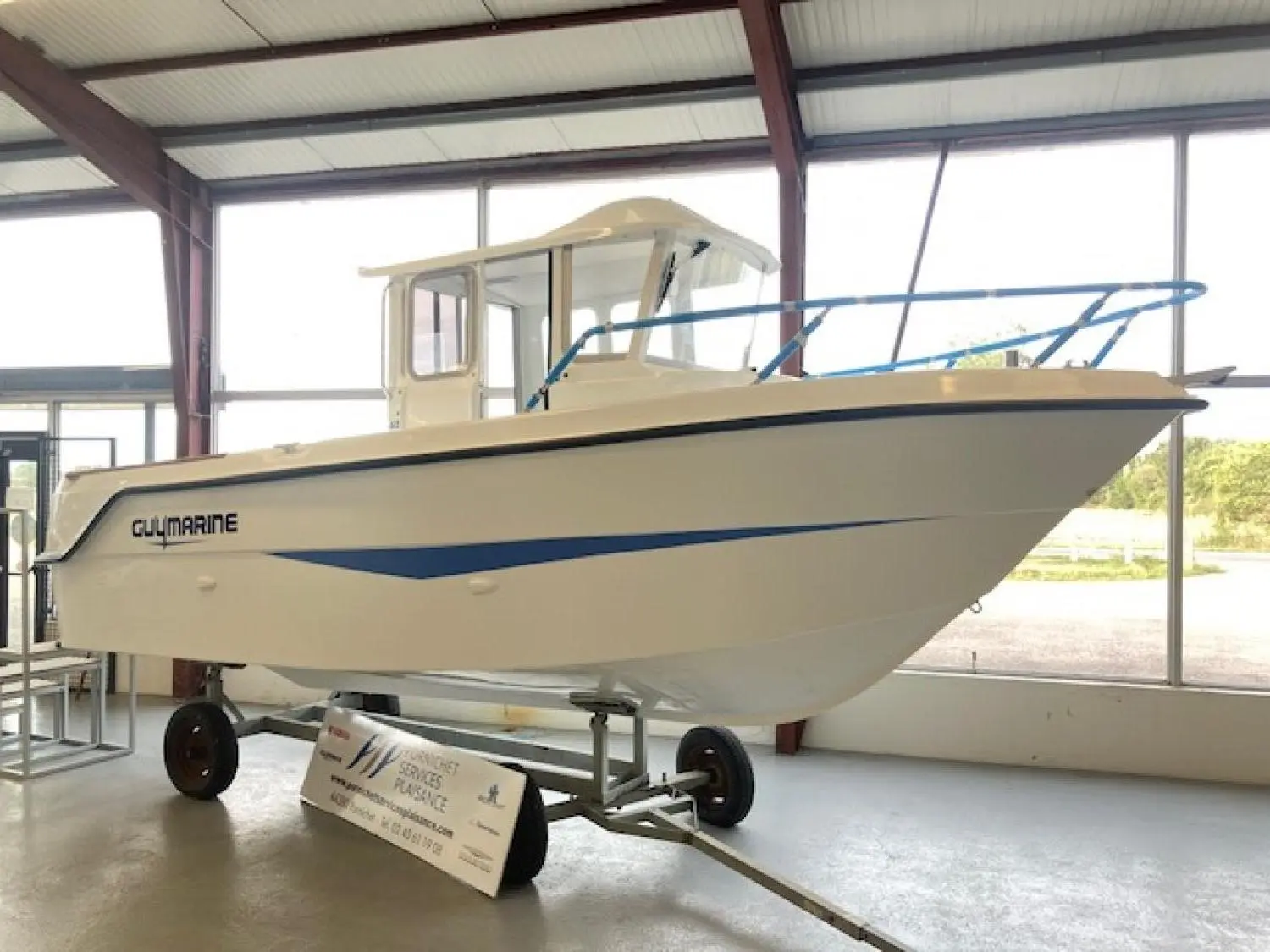 Guymarine Antioche 650 Chalutier — Bateau à cabine présenté sur remorque dans un espace intérieur vitré.