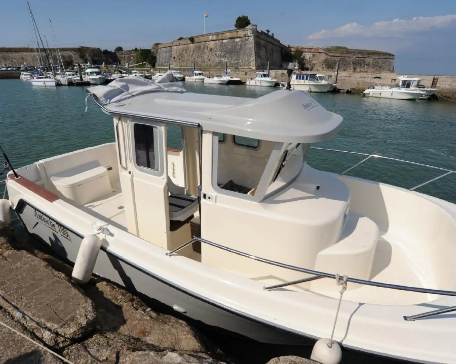 Guymarine Antioche 700 HB Chalutier — Bateau à cabine blanche amarré dans un port, devant une fortification.