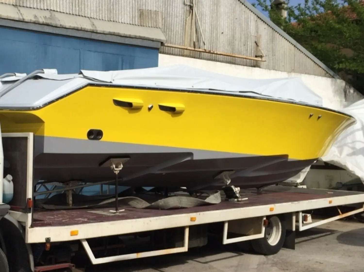 Offshore Marine Monte Carlo 30 — Bateau jaune et blanc bâché, posé sur une remorque devant un hangar.