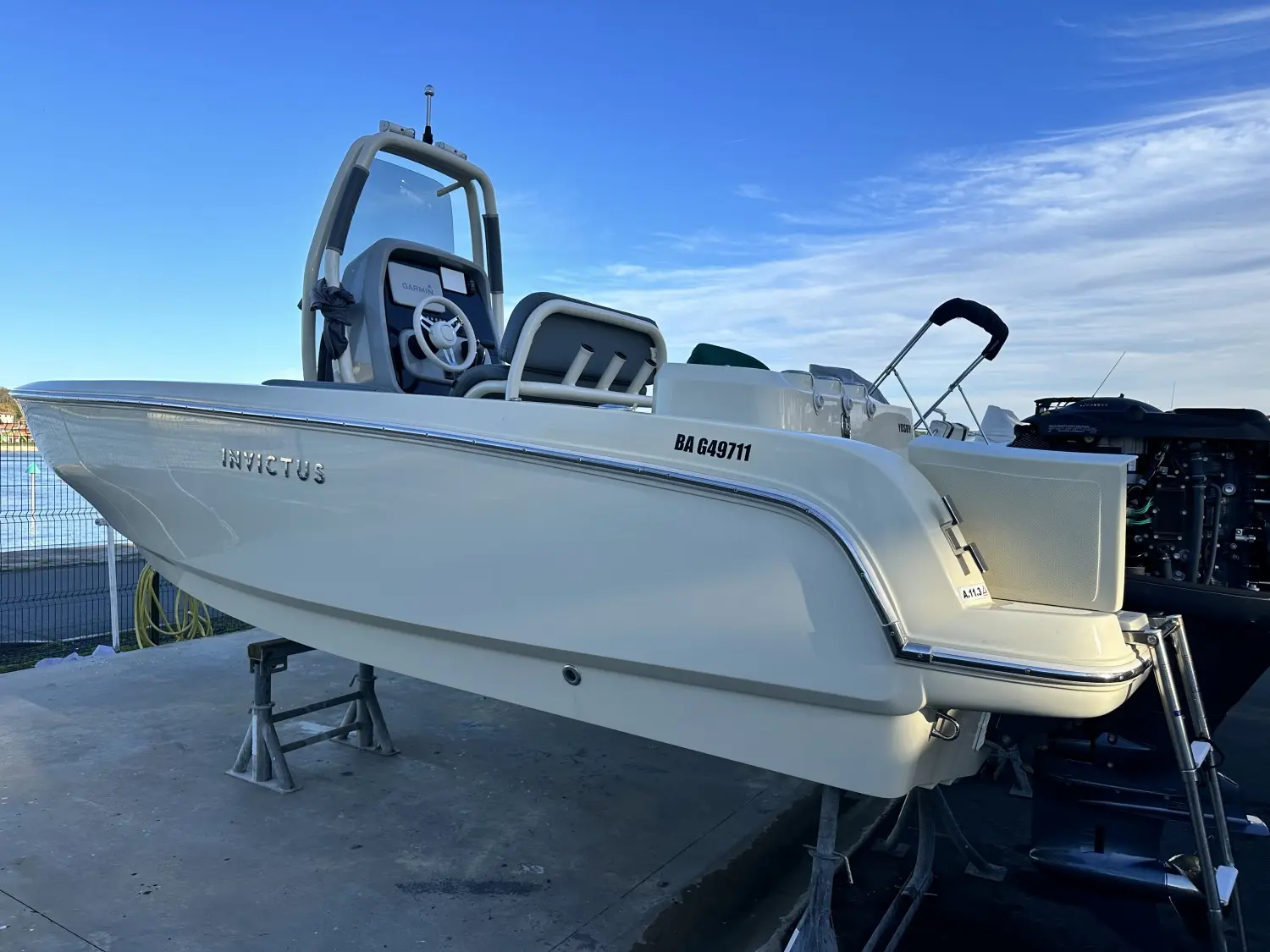Invictus 200 HX — Bateau blanc vu de profil sur supports, avec console centrale et moteur hors-bord.