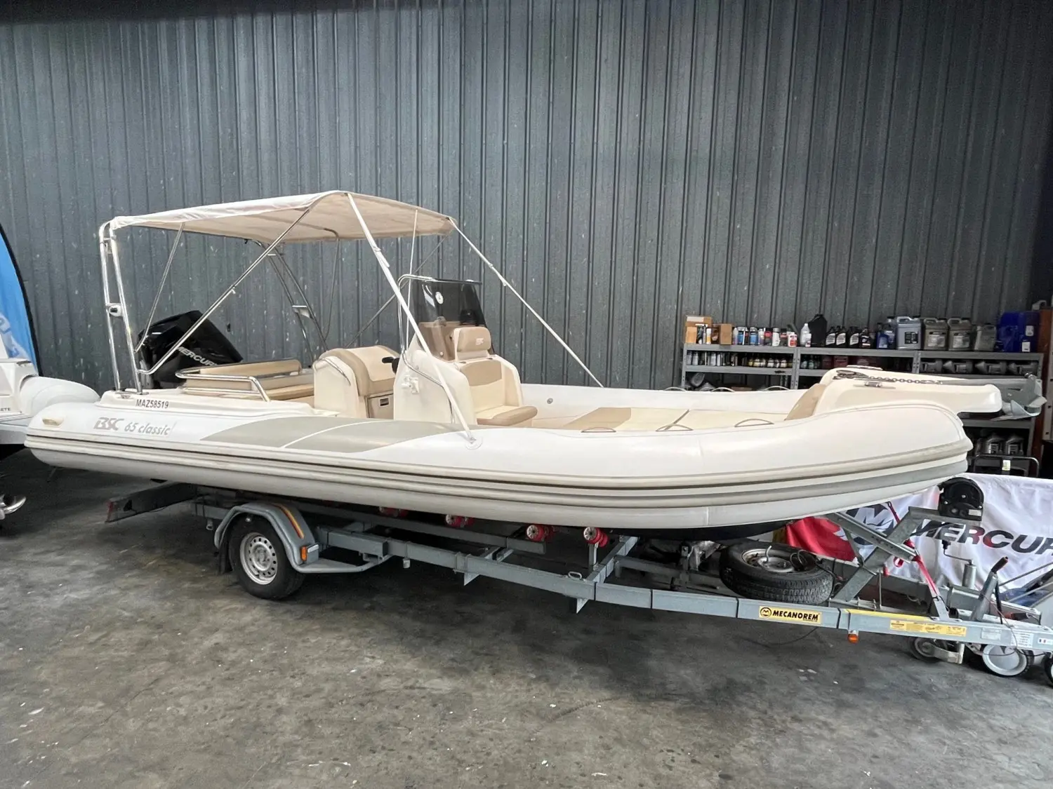 BSC 65 — Bateau pneumatique blanc vu de profil dans un hangar, avec console et taud.