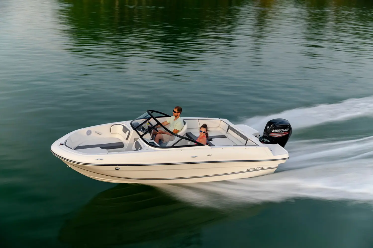 Bayliner VR4 — Bateau à moteur blanc naviguant sur l’eau, vu de trois quarts avec deux occupants.