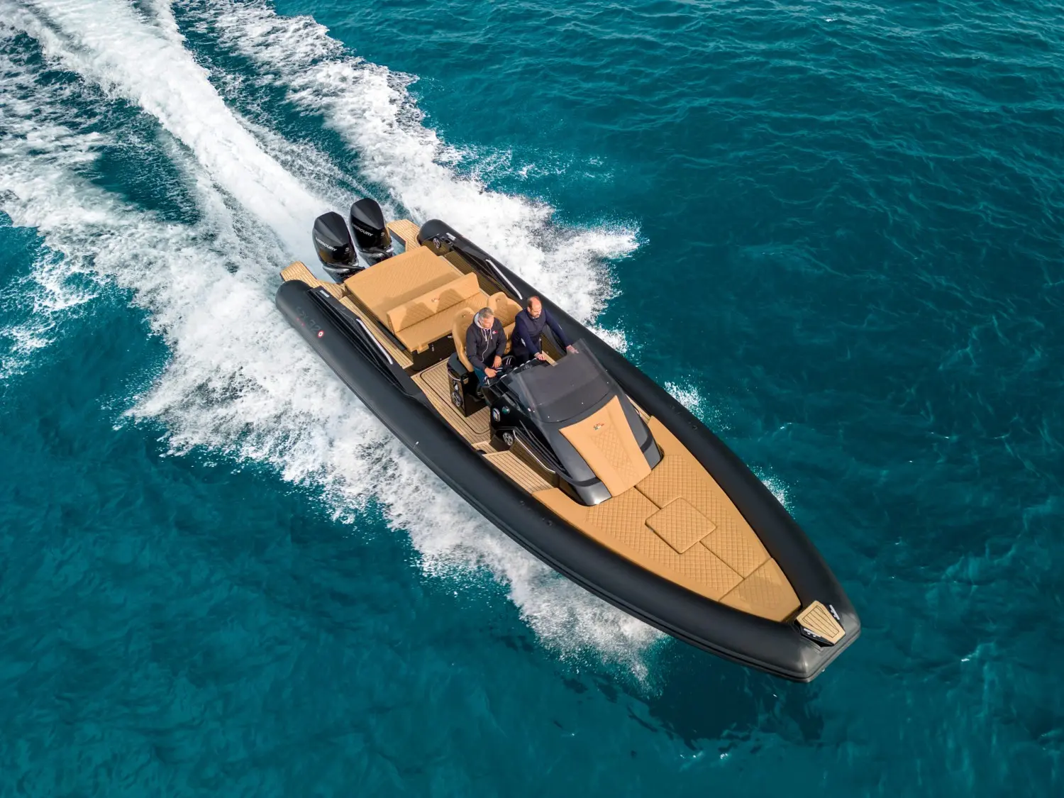 SPX Rib 32 Sport — Vue aérienne d’un semi-rigide noir et beige naviguant sur une mer turquoise.