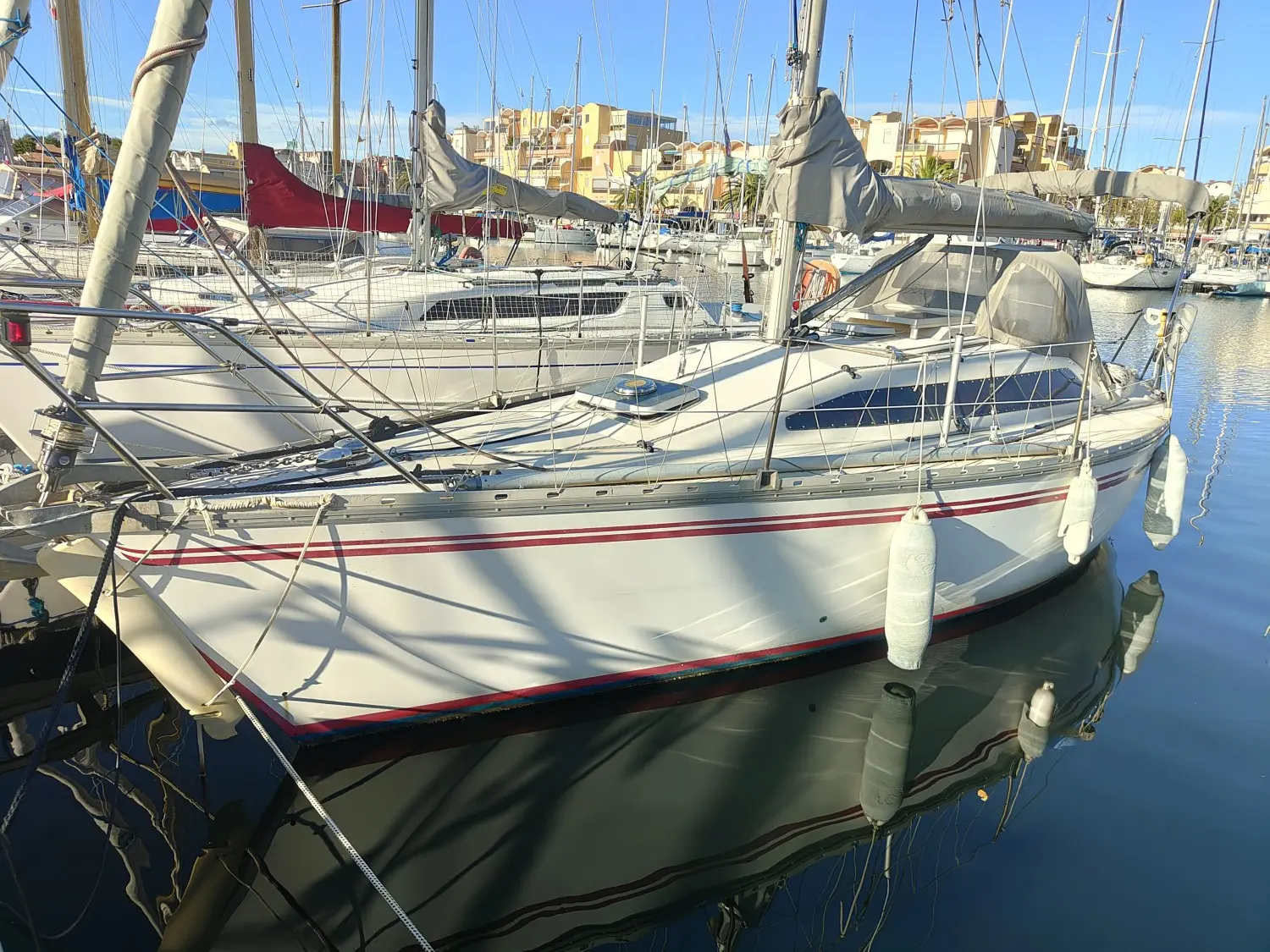 Jeanneau Rush — Voilier blanc à liserés rouges amarré dans un port de plaisance.