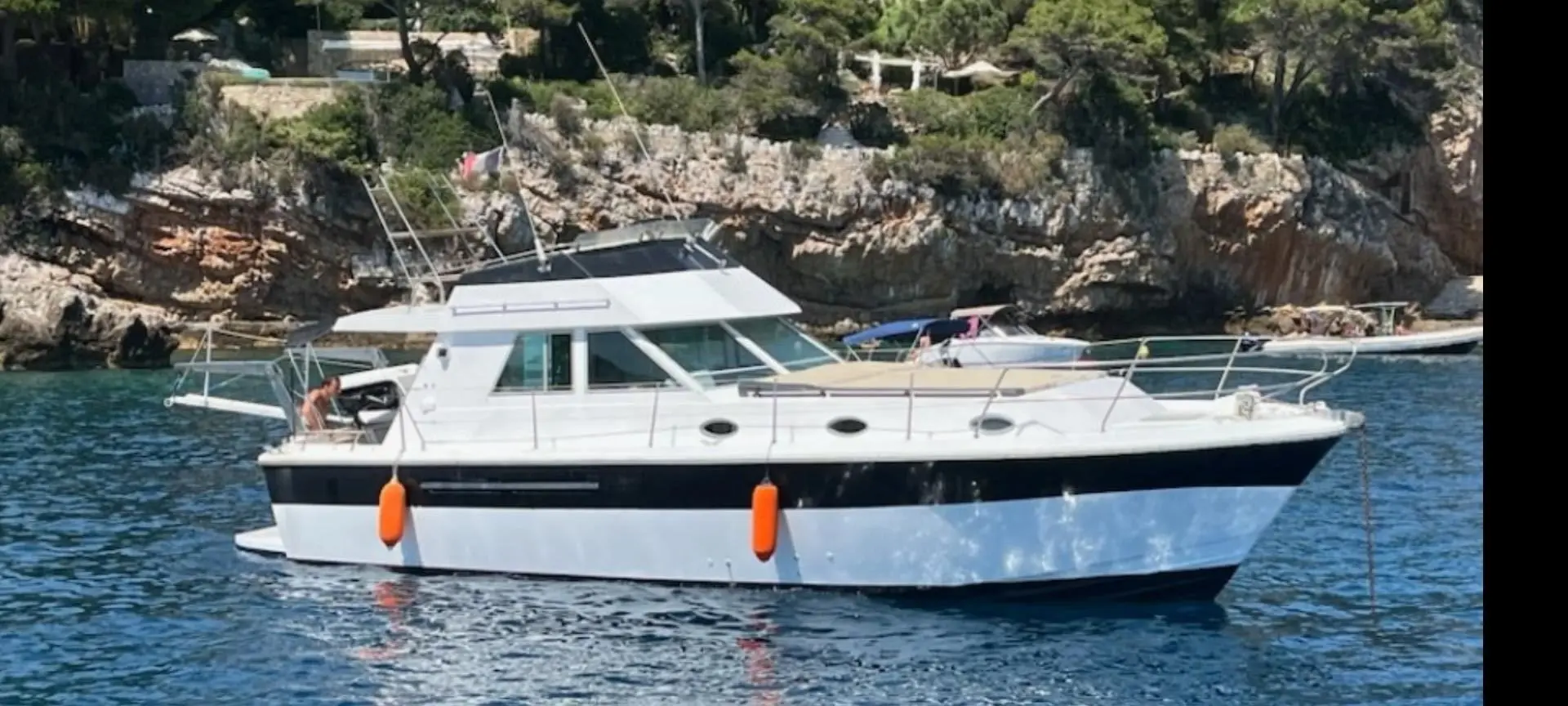 Princess 37 — Bateau à moteur blanc et bleu photographié de profil dans une crique rocheuse.