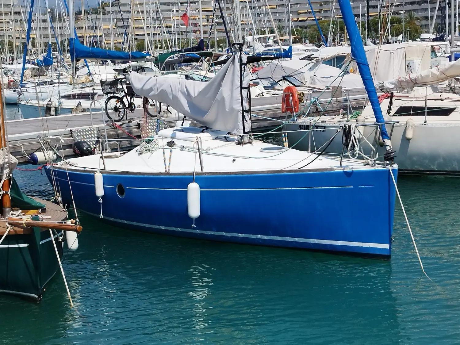 Beneteau First 210 — Voilier bleu amarré dans un port, vu de côté.