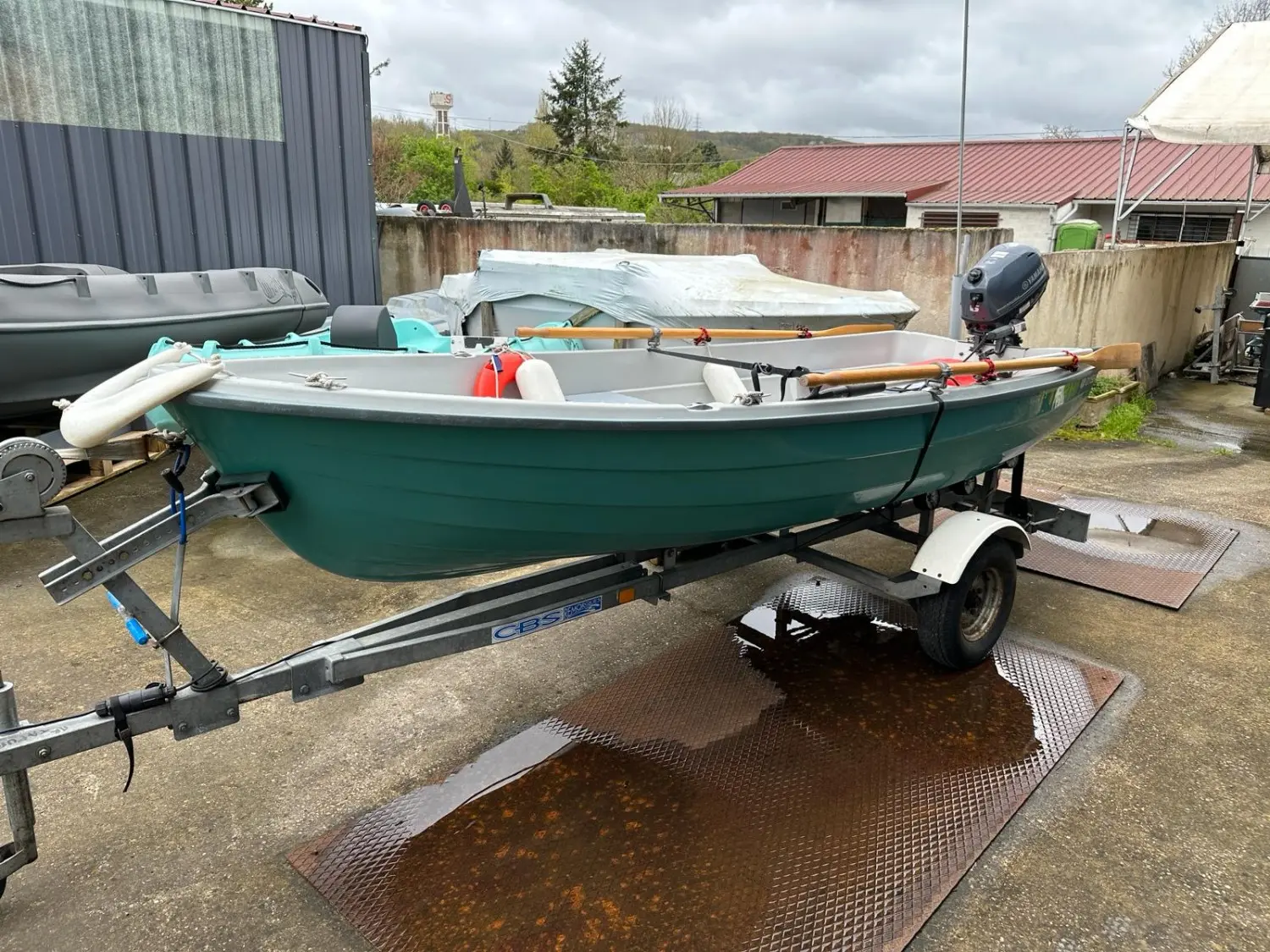 Terhi 385 — Bateau vert sur remorque, équipé d’un moteur hors-bord, dans une cour extérieure.