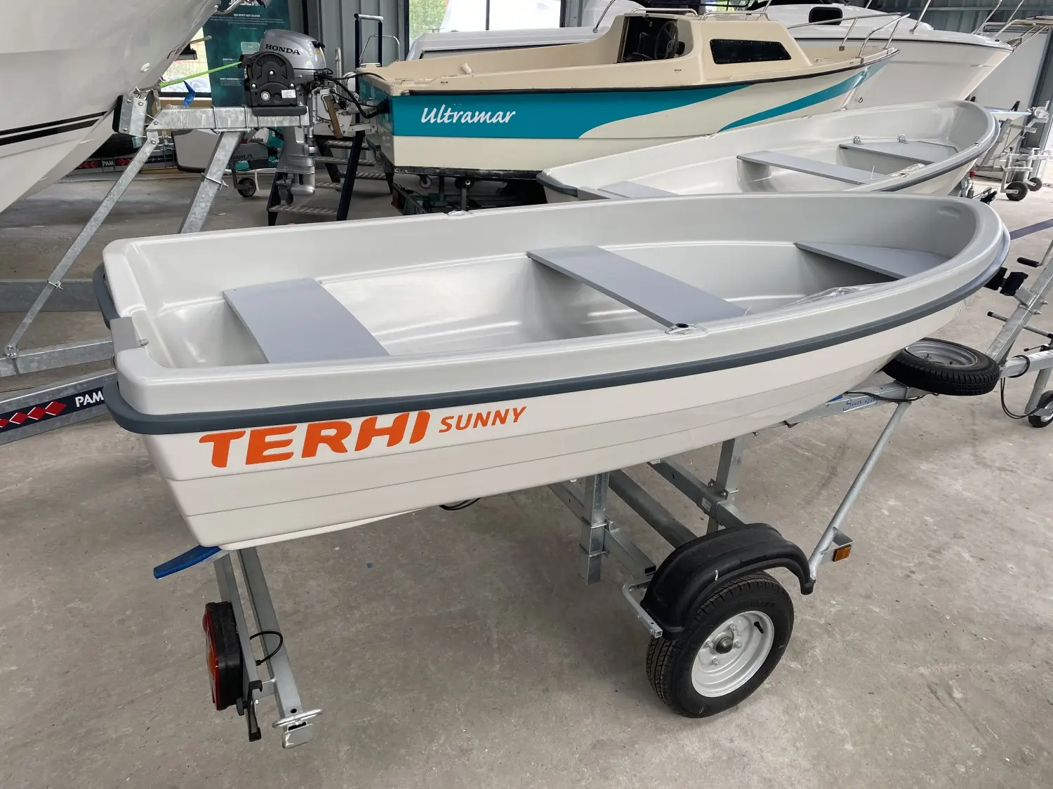 Terhi Sunny — Petit bateau blanc sur remorque, photographié en intérieur, avec deux bancs gris.