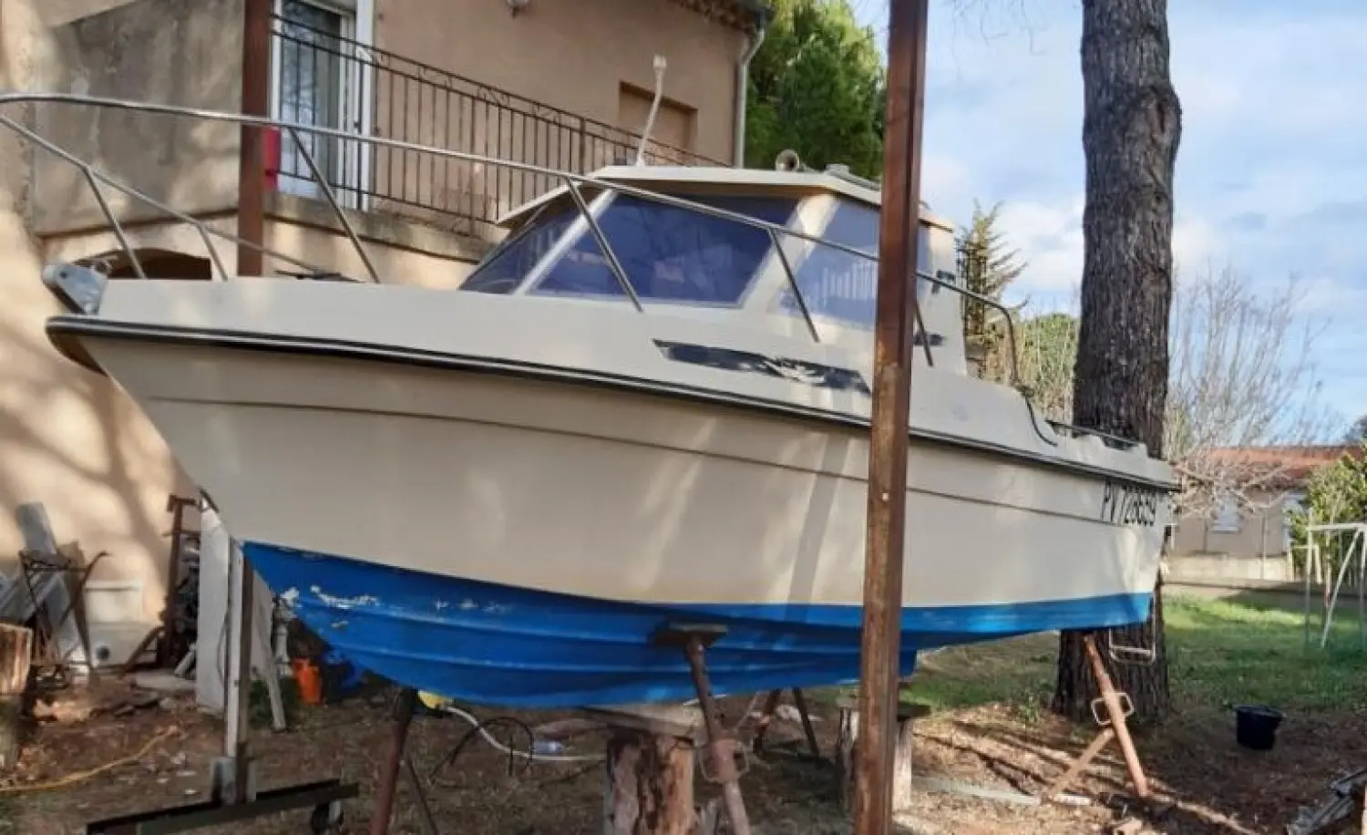 Guymarine GM 560 — Bateau à moteur blanc et bleu posé sur bers dans un jardin.