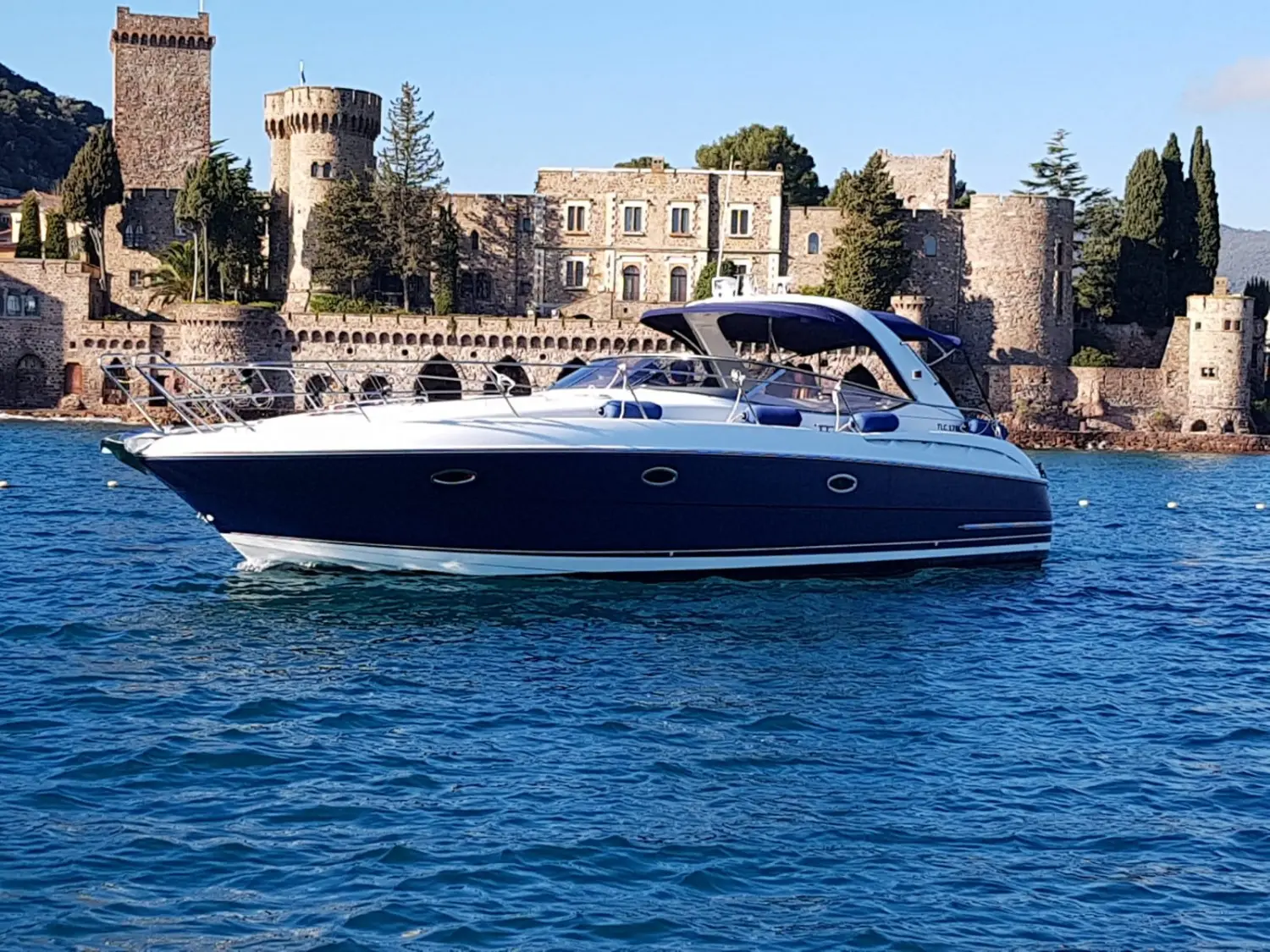 Bavaria 37 — Bateau à moteur bleu et blanc vu de trois quarts sur l’eau, devant un château.