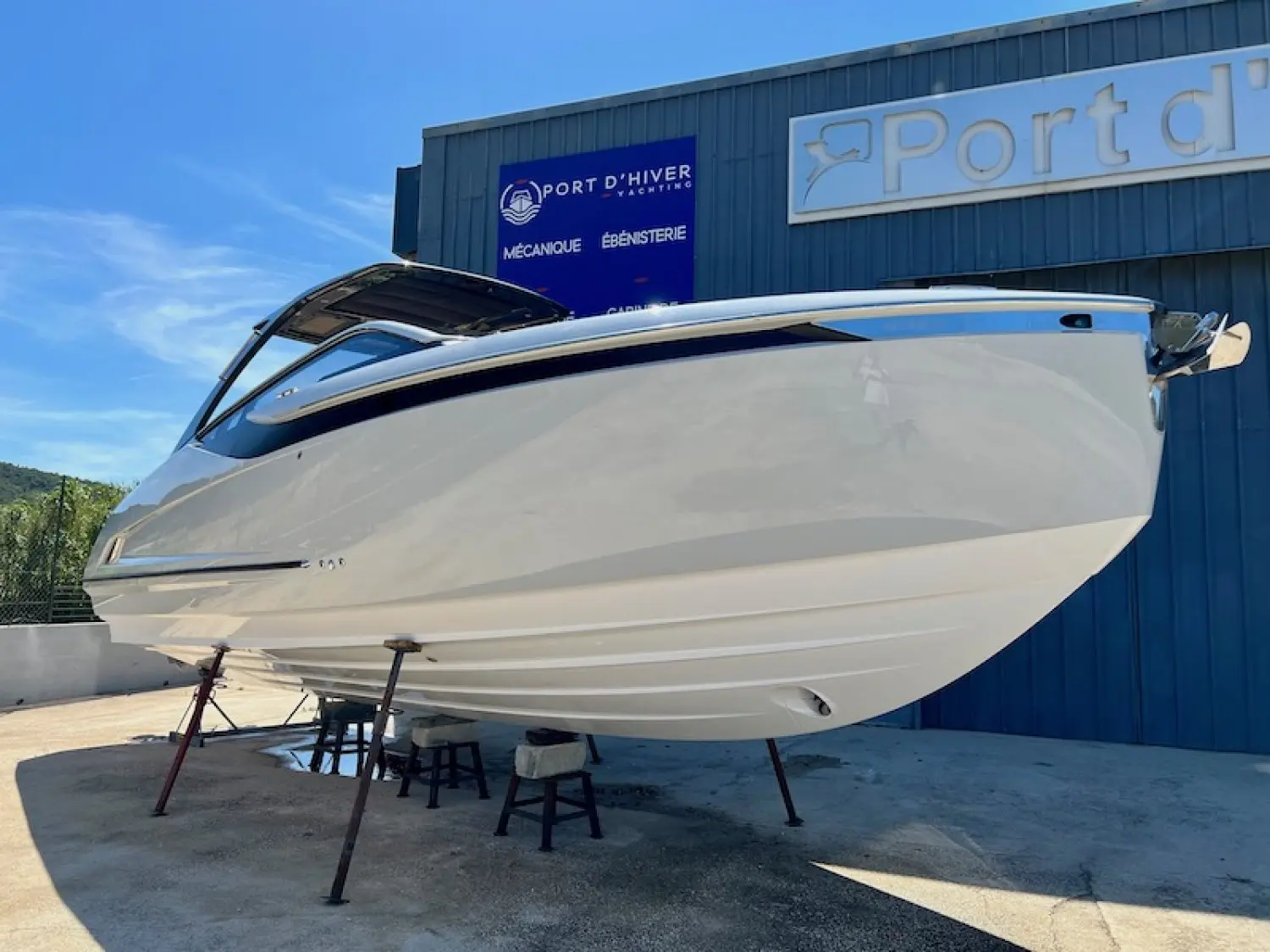 Fairline F-Line 33 — Vue rapprochée de la coque blanche d’un bateau sur berceau devant un bâtiment nautique.