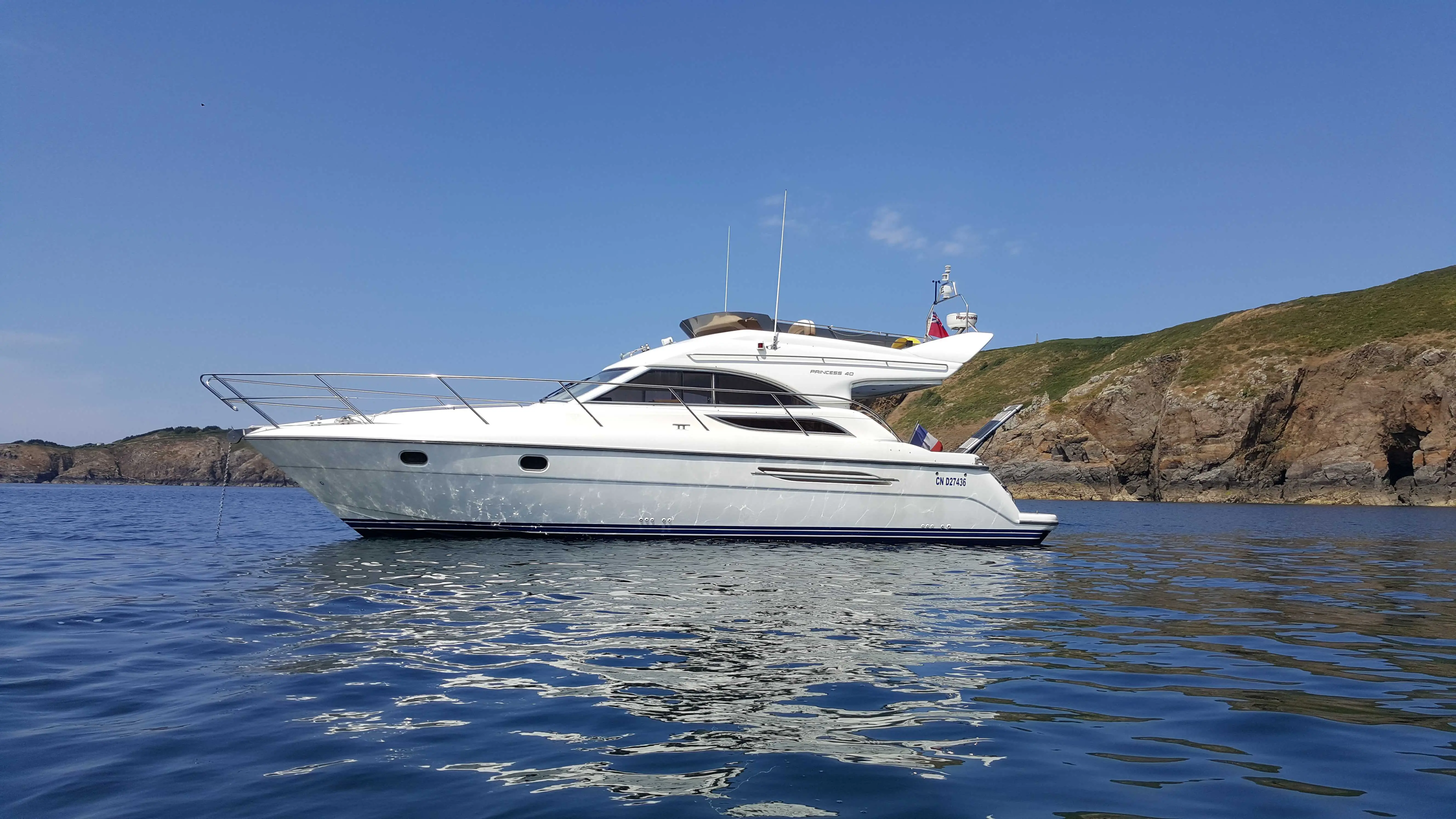 Princess 40 — Bateau à moteur blanc vu de profil sur une mer calme, près d’une côte rocheuse.