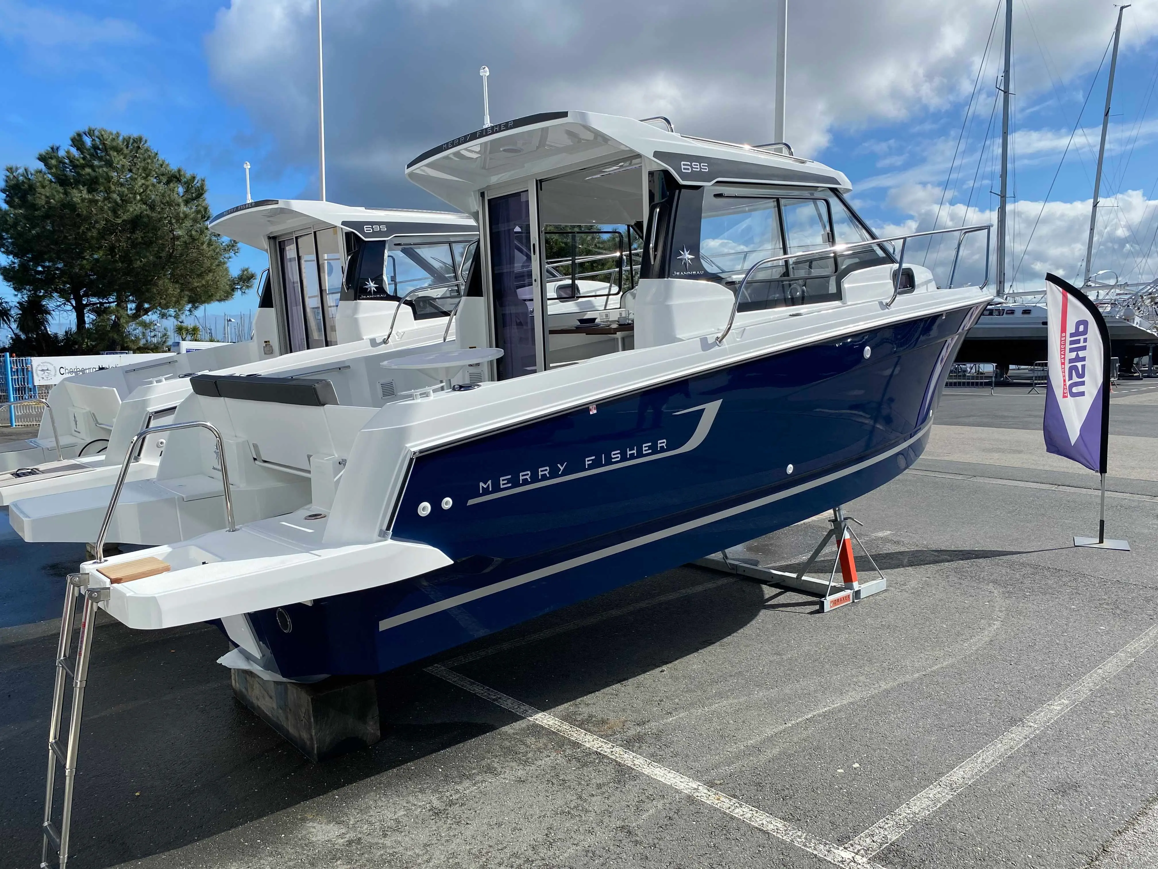 Jeanneau Merry Fisher 695 — Bateau à moteur bleu et blanc exposé à terre sur un stand nautique.