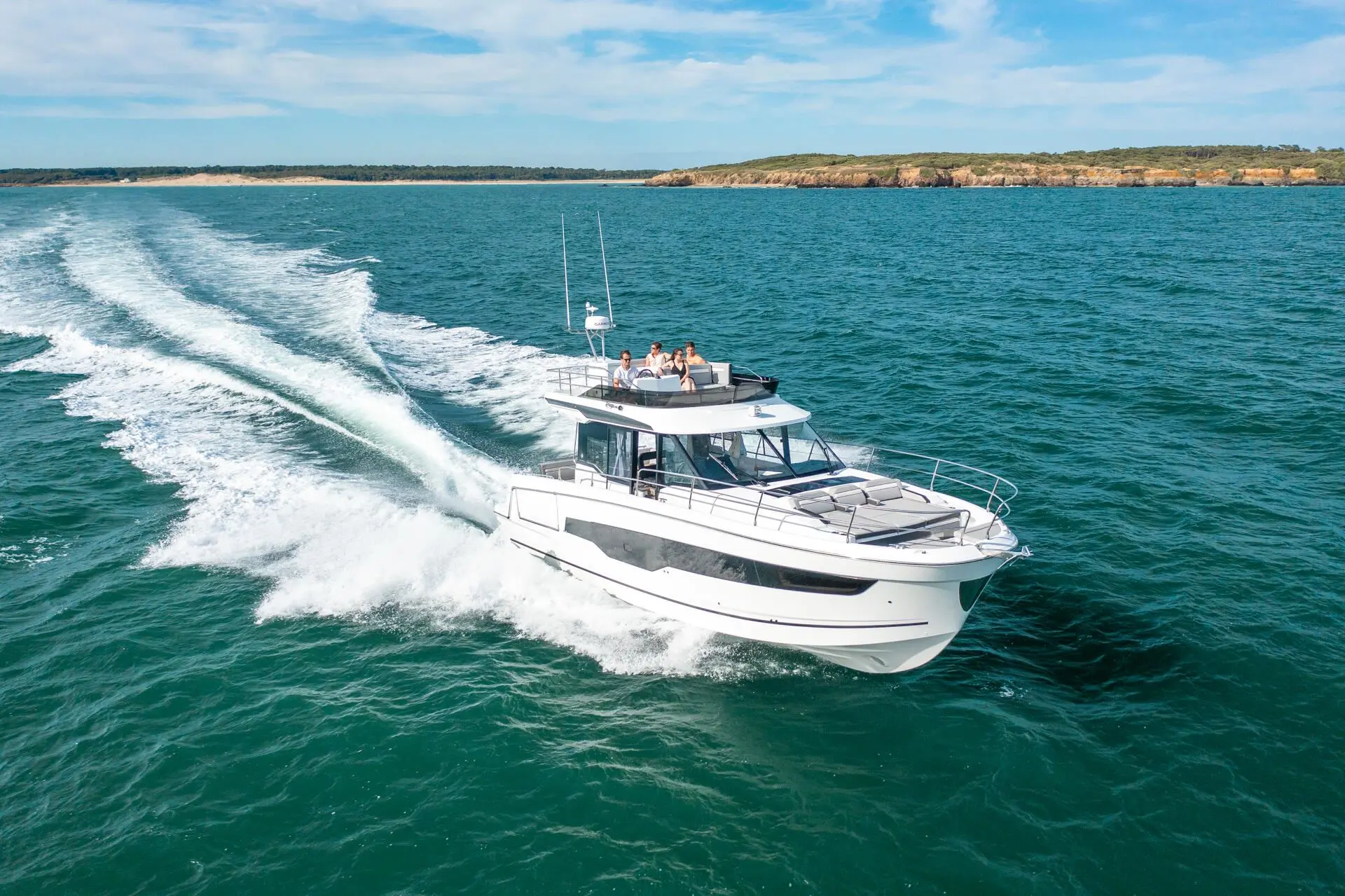 Jeanneau Merry Fisher 1295 Fly — Bateau à moteur blanc naviguant près d’une côte rocheuse, vu de trois quarts.