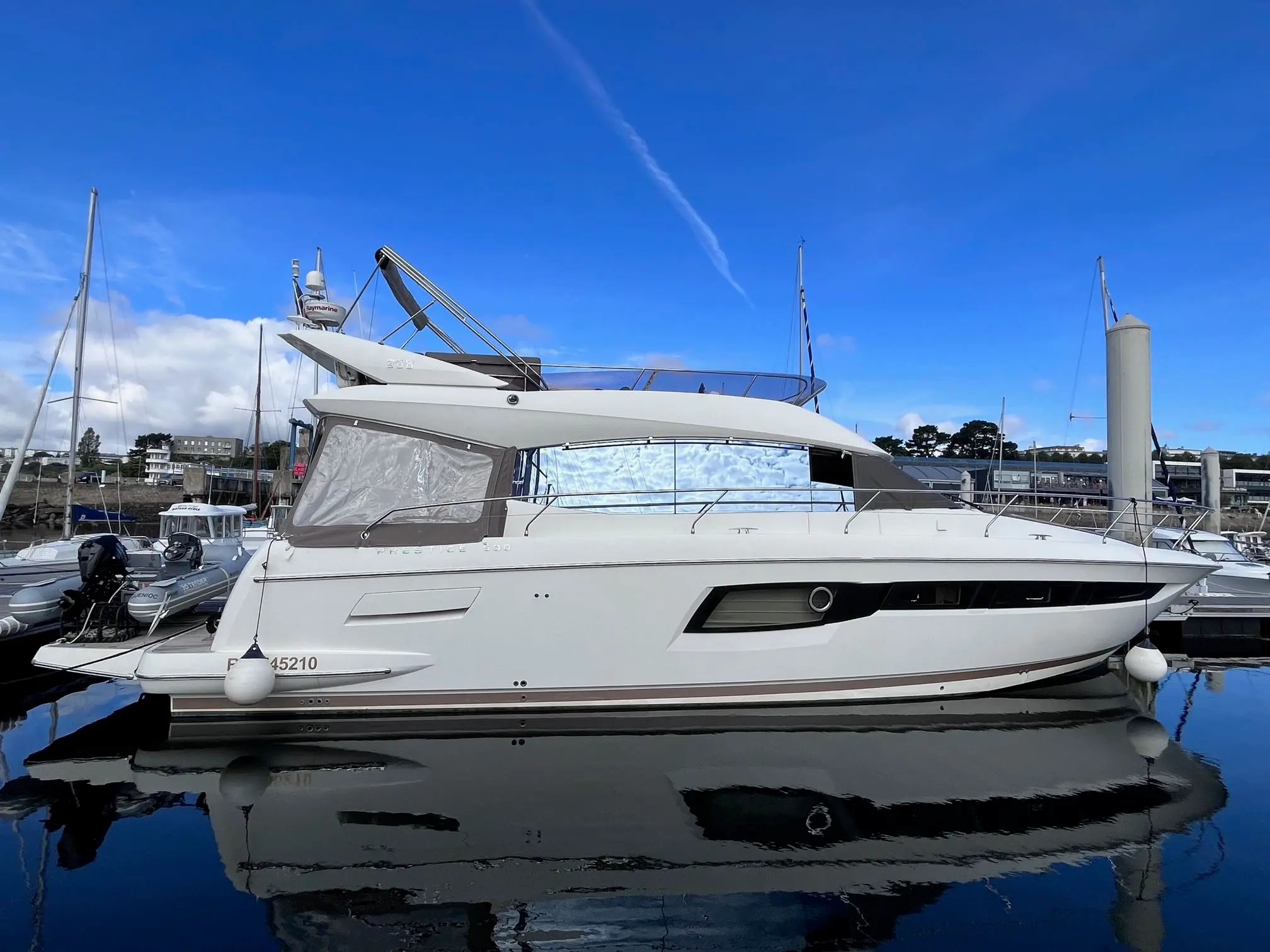 Jeanneau Prestige 500 Fly — Bateau à moteur blanc photographié de profil dans une marina, amarré sur l’eau.