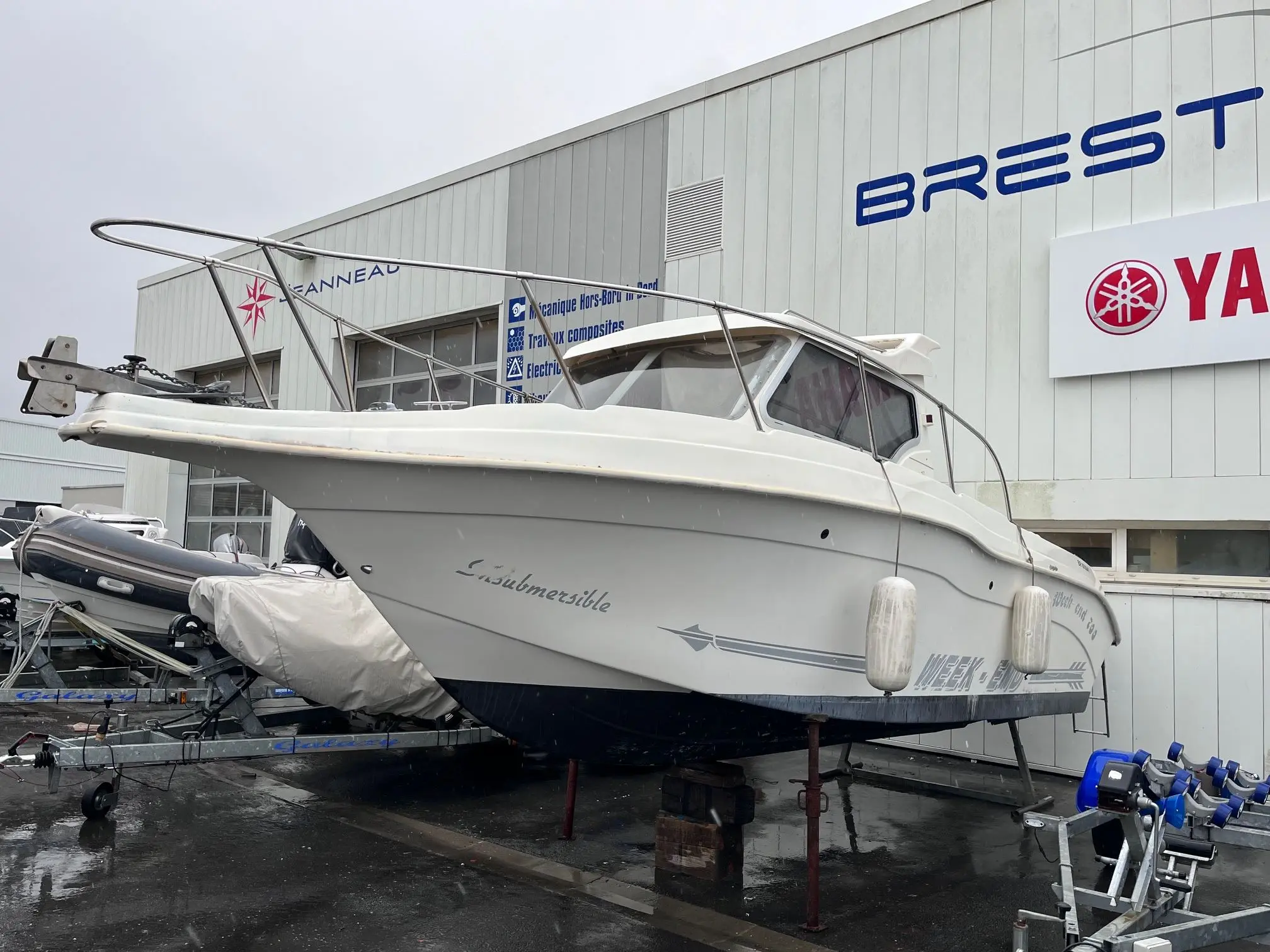 Ultramar 700 Week End — Bateau blanc à cabine photographié sur berceau devant un bâtiment nautique.