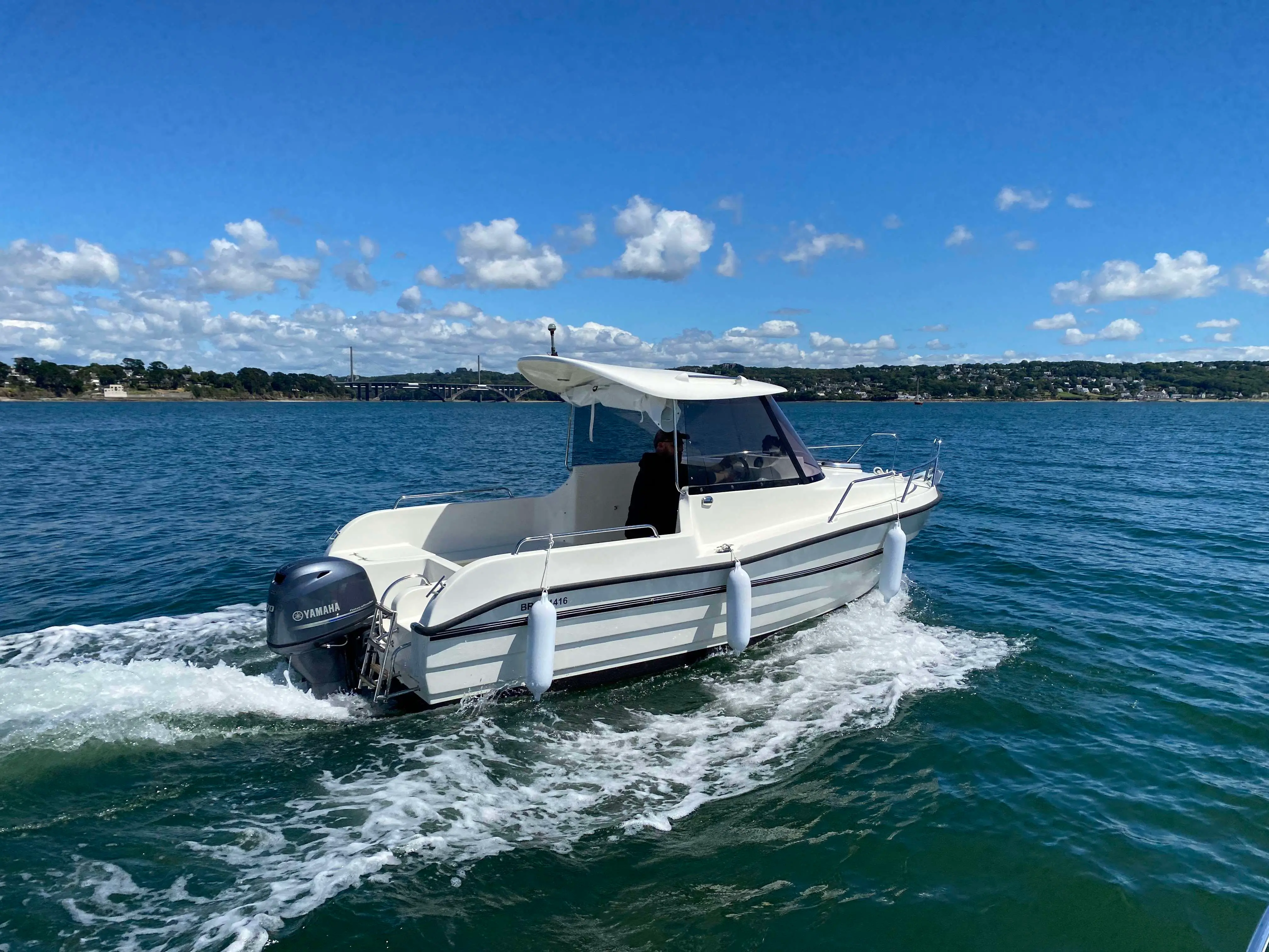 Texas 540 Pilothouse — Bateau à moteur blanc vu de trois quarts arrière, naviguant sur une étendue d’eau.