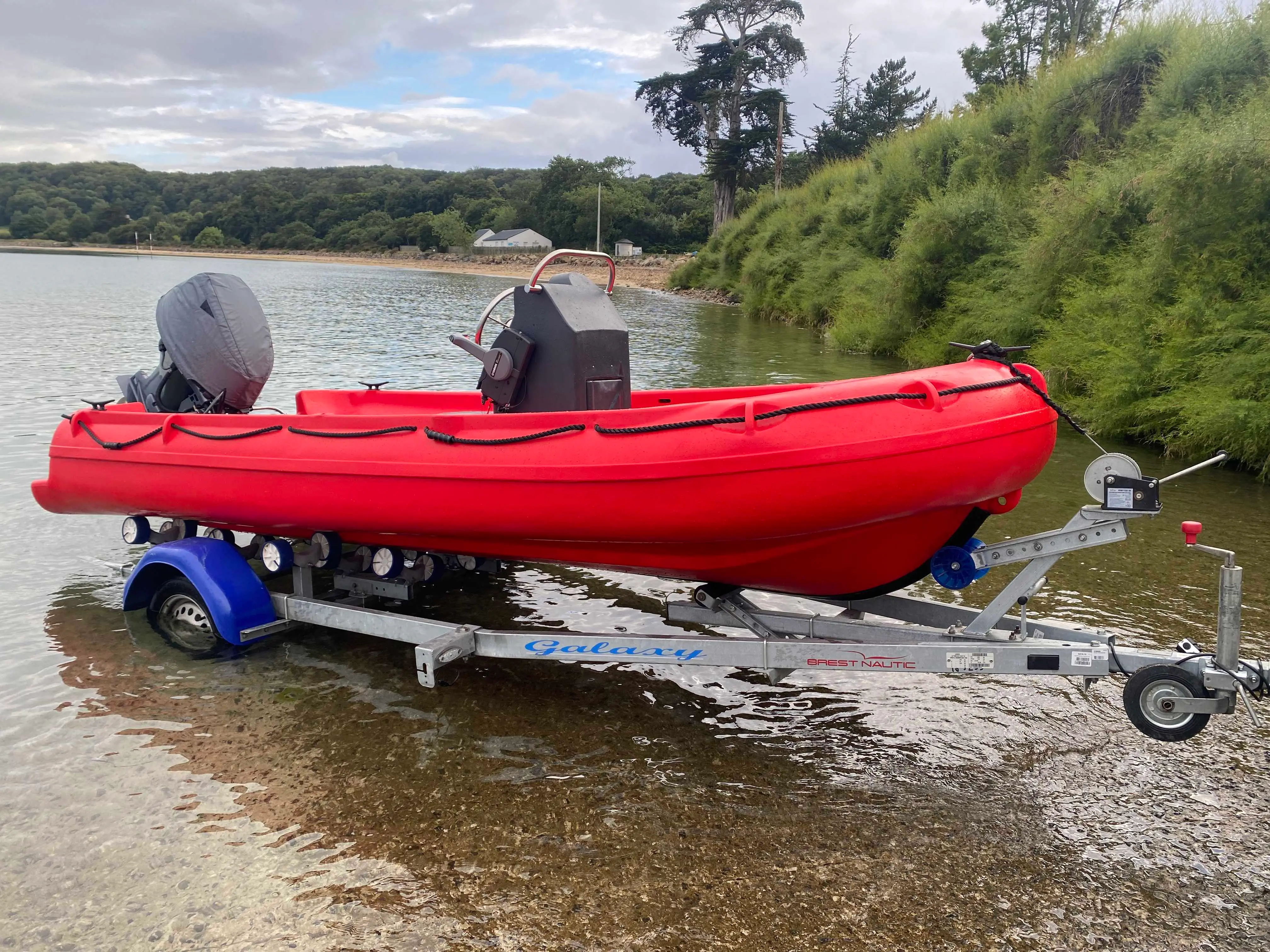 Fun Yak Secu 13 — Bateau pneumatique rouge avec moteur hors-bord, sur une remorque au bord de l’eau.
